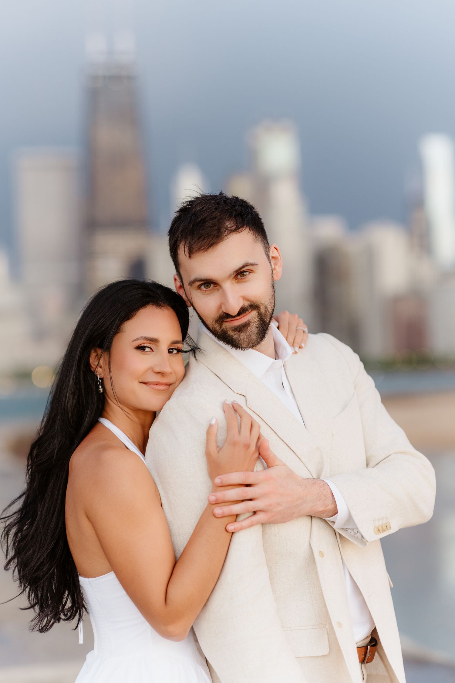 Couple posing together on Chicago lakefront pier, both looking at camera with city skyline behind them.