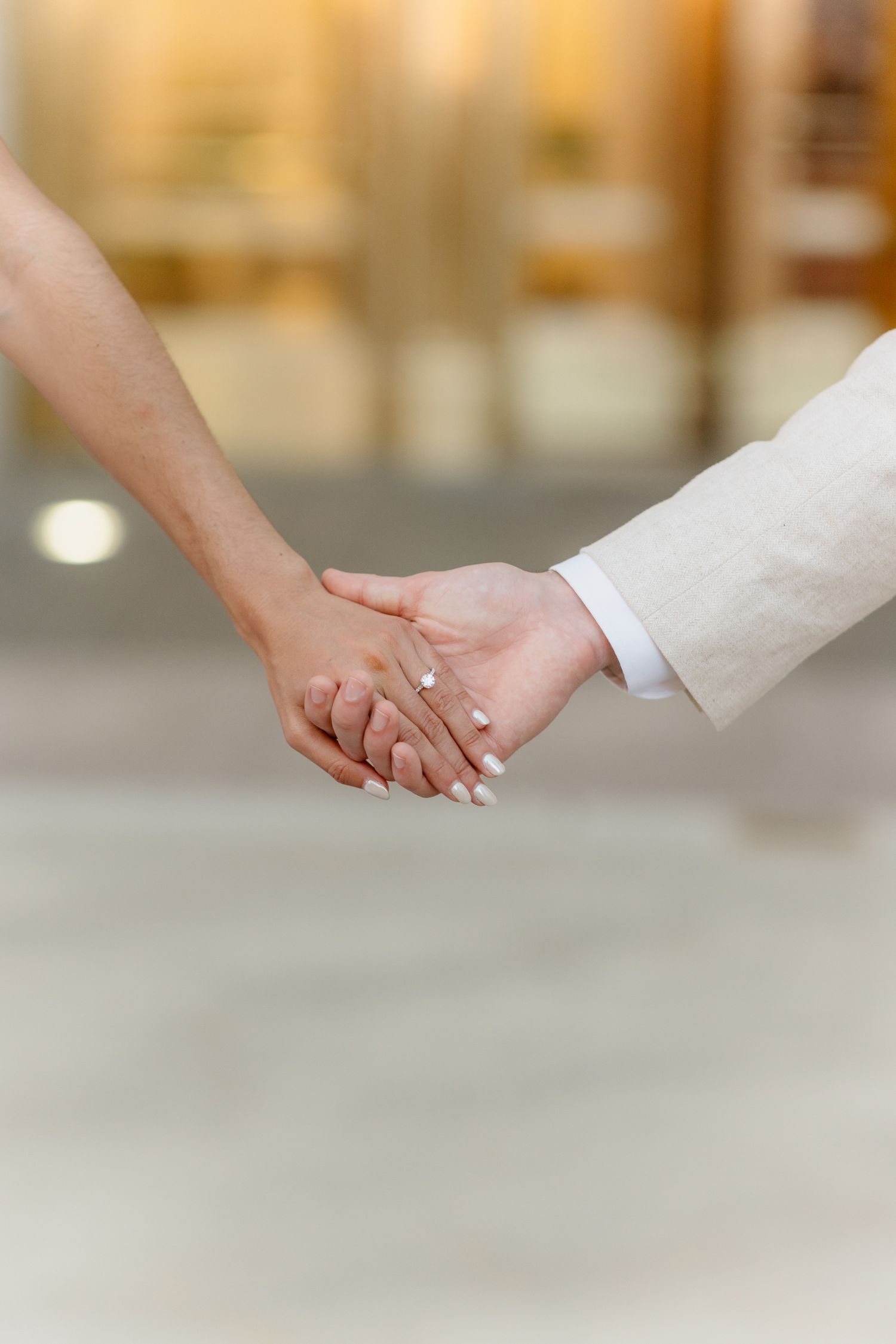 Detail shot of engaged couple holding hands with diamond ring and white manicure.