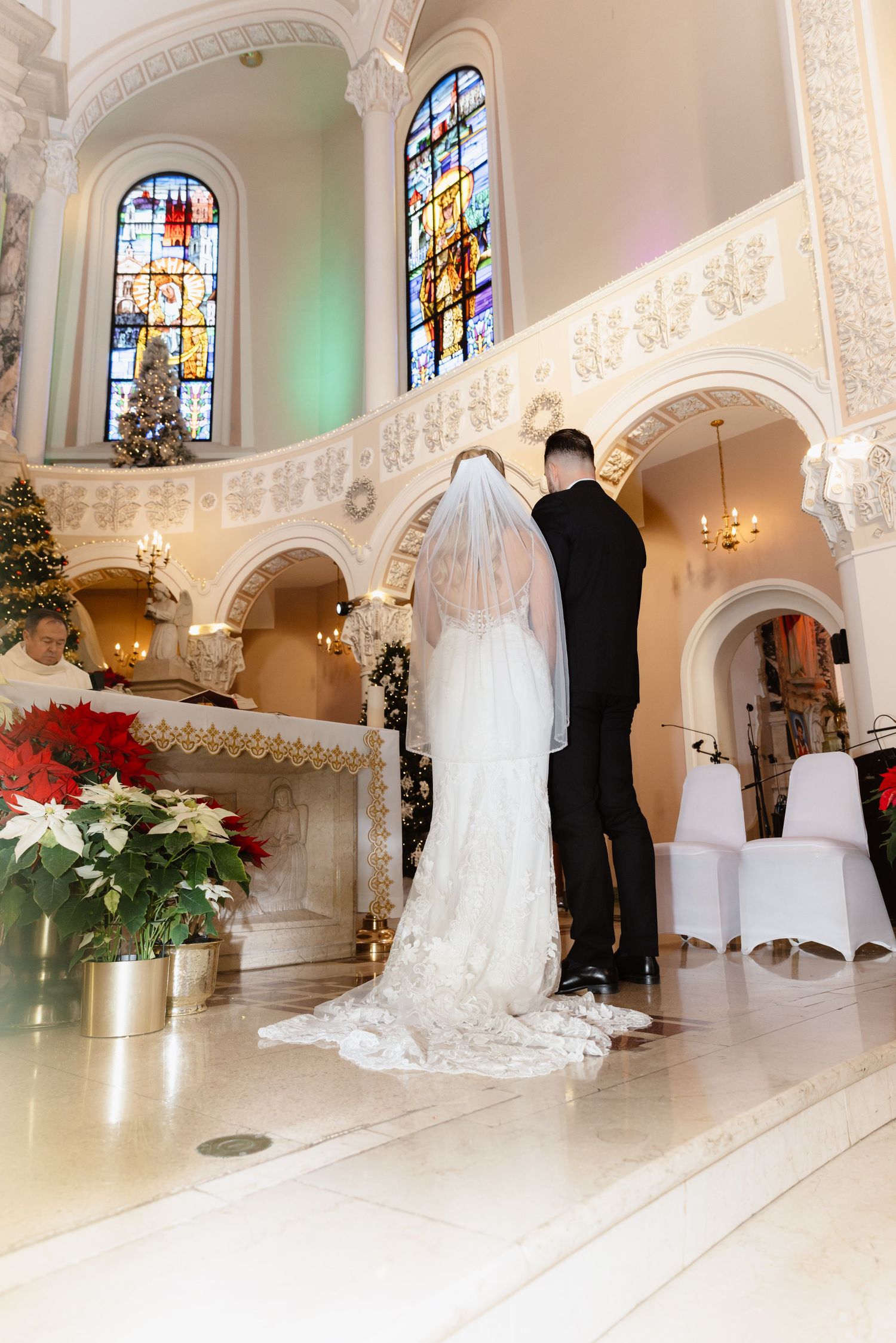 Bride and groom standing at ornate church altar with stained glass windows and Christmas decor.