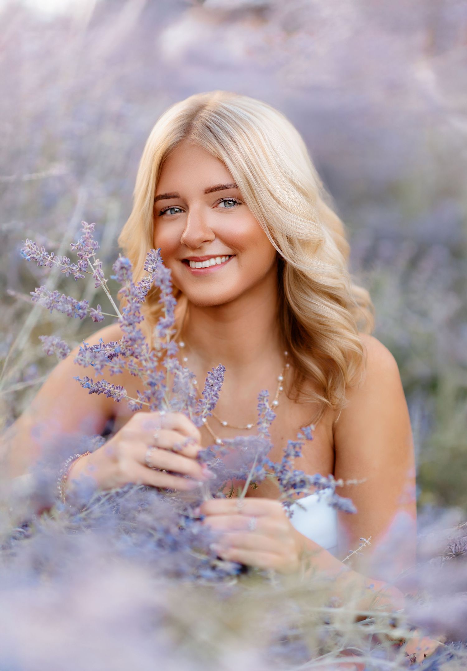 Beautiful blonde woman holding purple lavender stems, smiling in a lavender field.