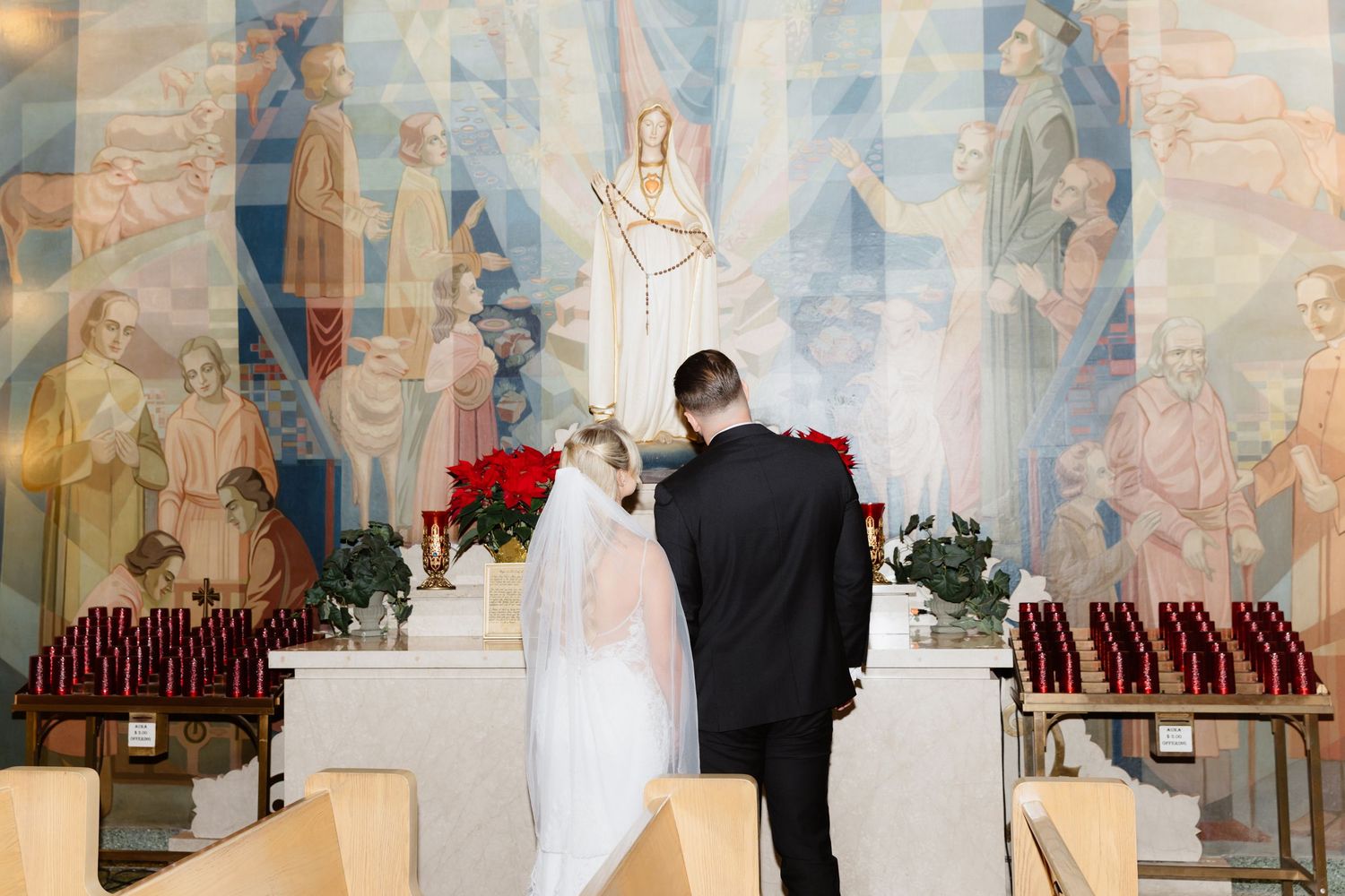 Wedding couple at altar with stunning religious fresco mural, red roses, and rows of votive candles.