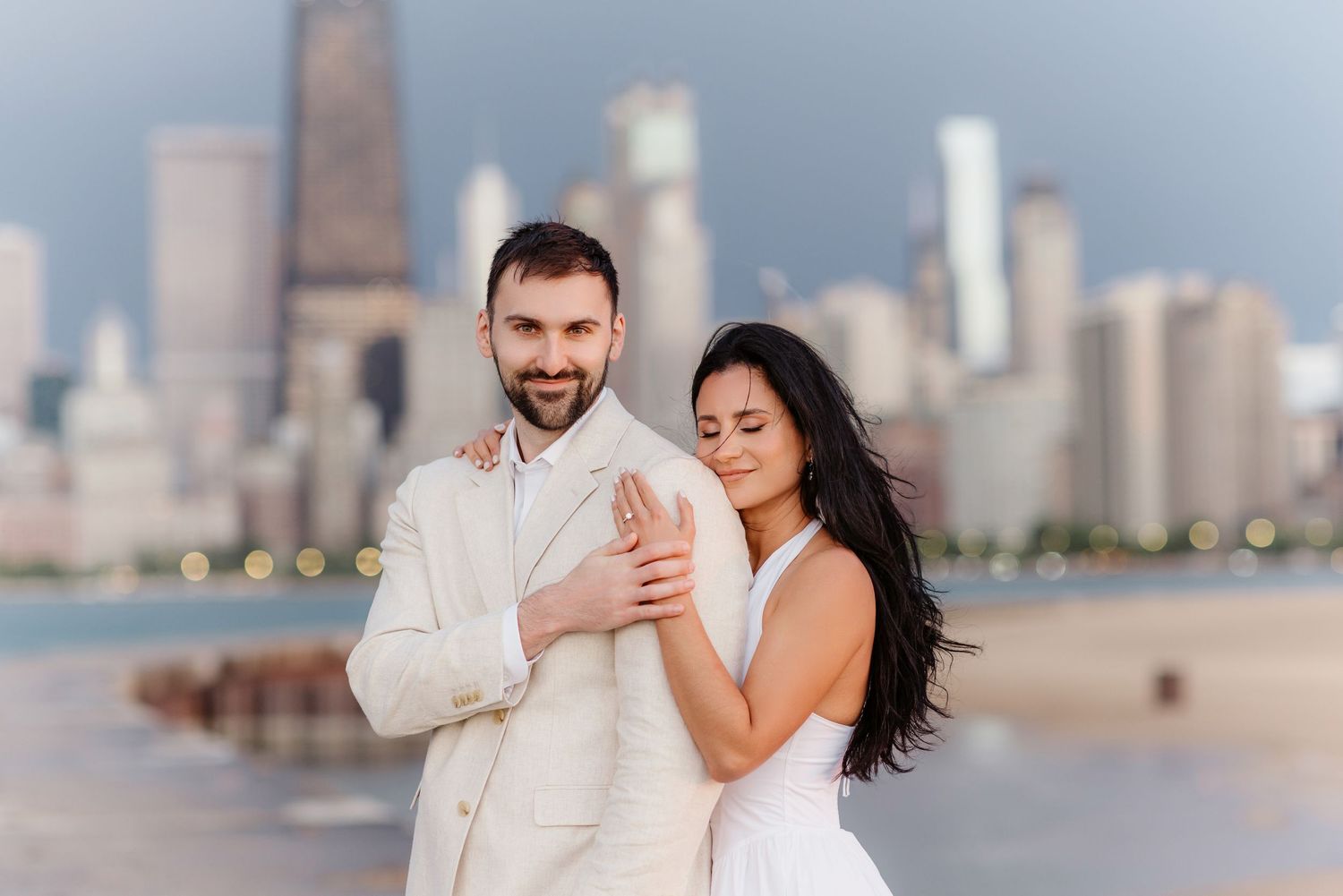 Smiling groom in cream suit with bride in white dress near Chicago lakefront.