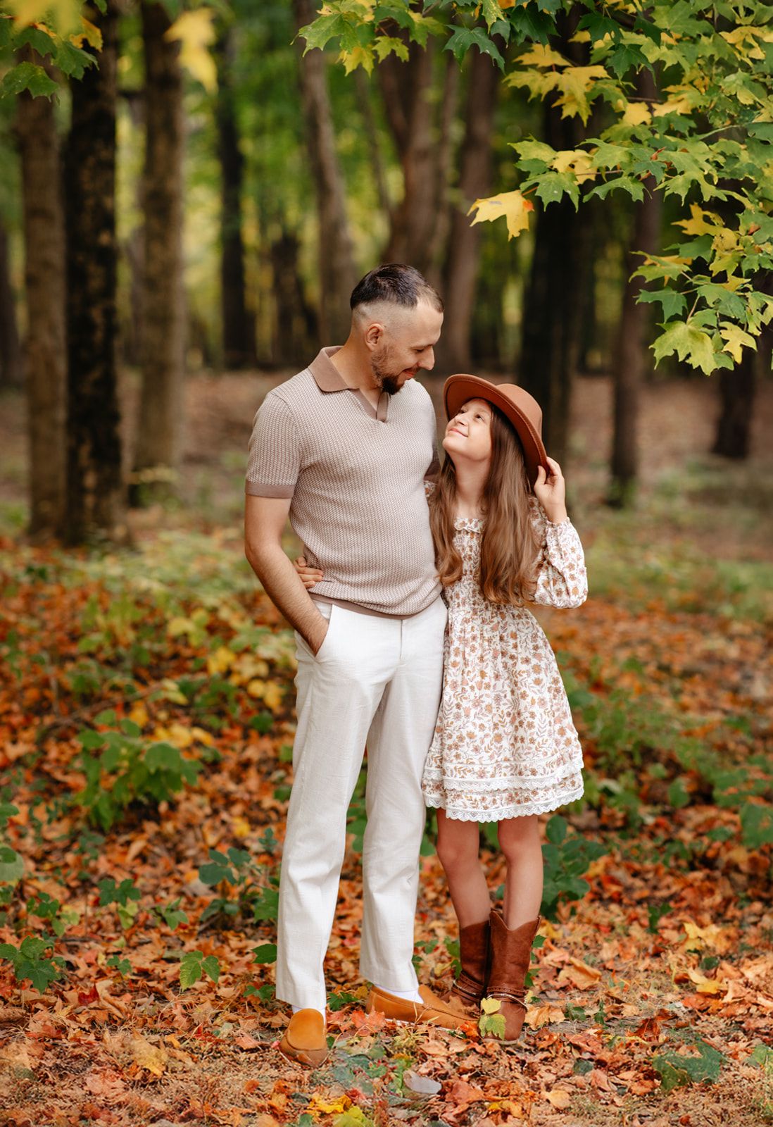 Father and daughter share a sweet moment in colorful autumn forest with fallen leaves.