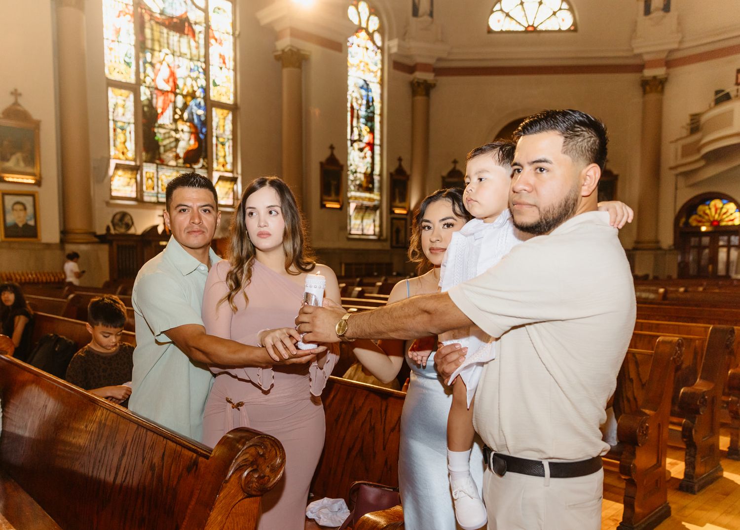Family gathered in a church holding a baptism candle during a christening ceremony.