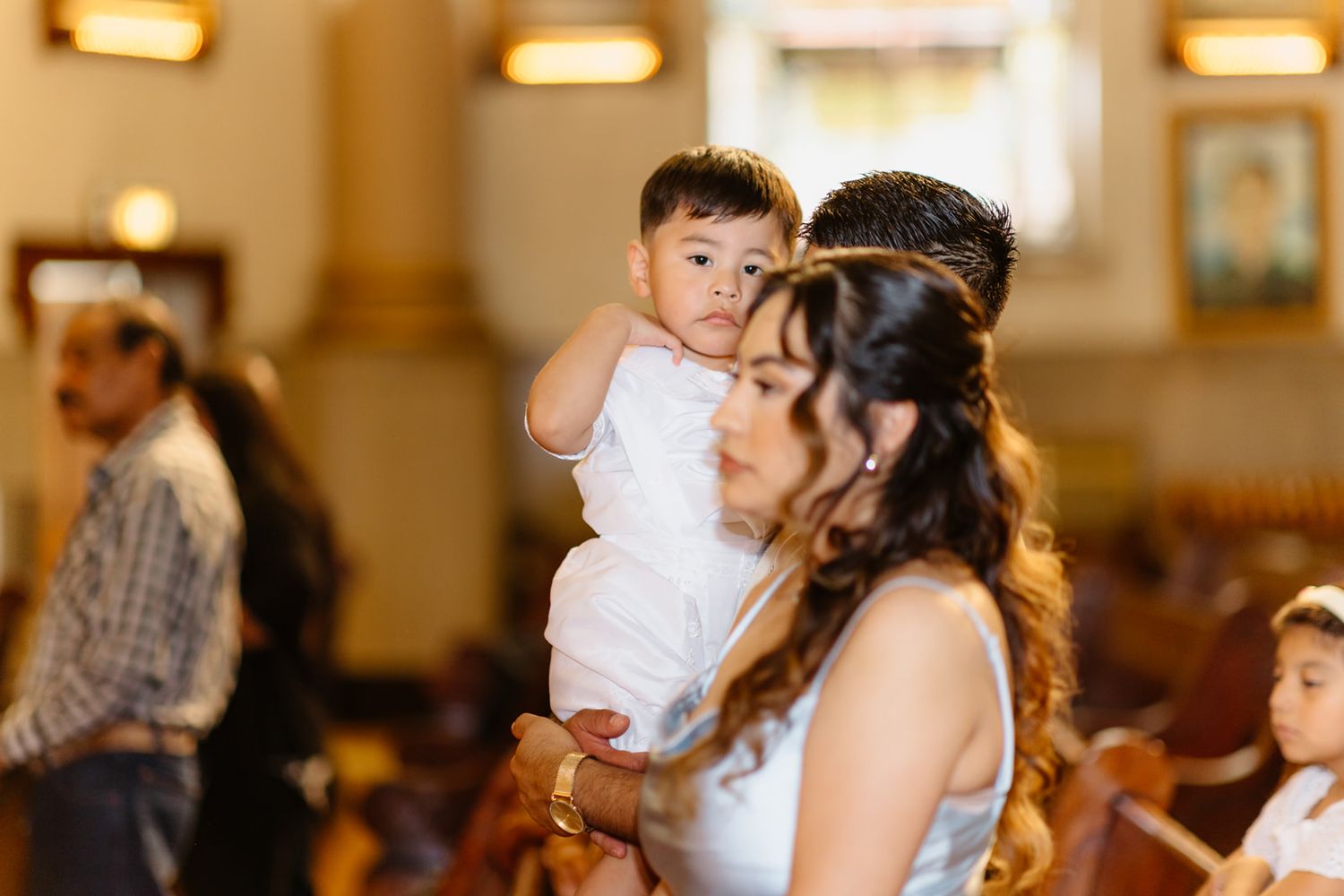 A mother in white holds her baby boy during a Catholic baptism ceremony inside a church.