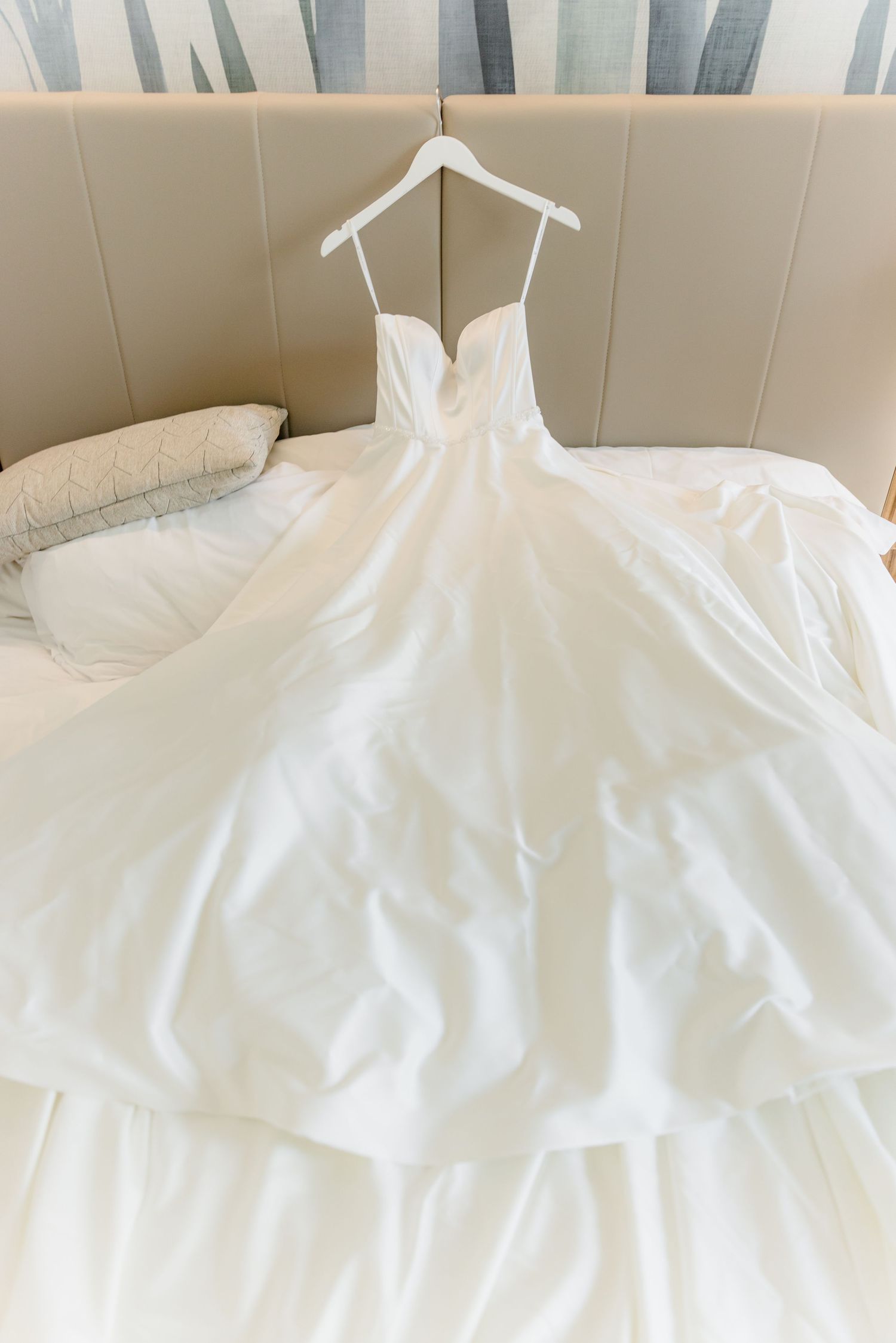 Elegant white ball gown wedding dress with sweetheart neckline displayed on hanger over hotel bed.