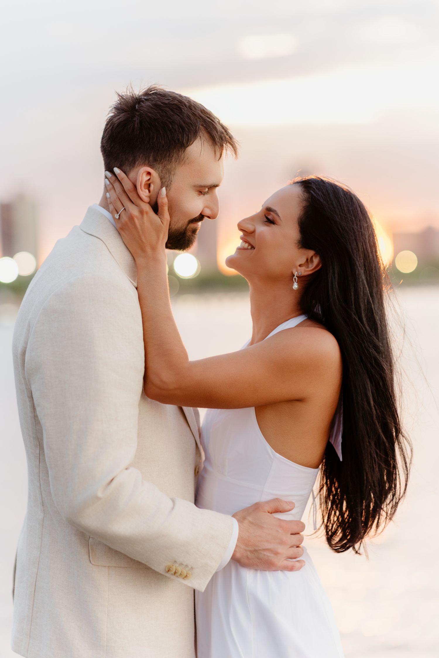 Laughing bride and groom embrace during romantic sunset photo session by lake.