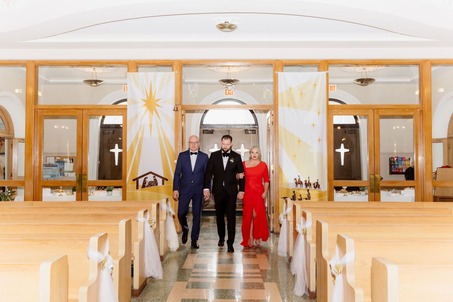 Groom walks down church aisle with parents in elegant wedding ceremony inside a bright chapel.