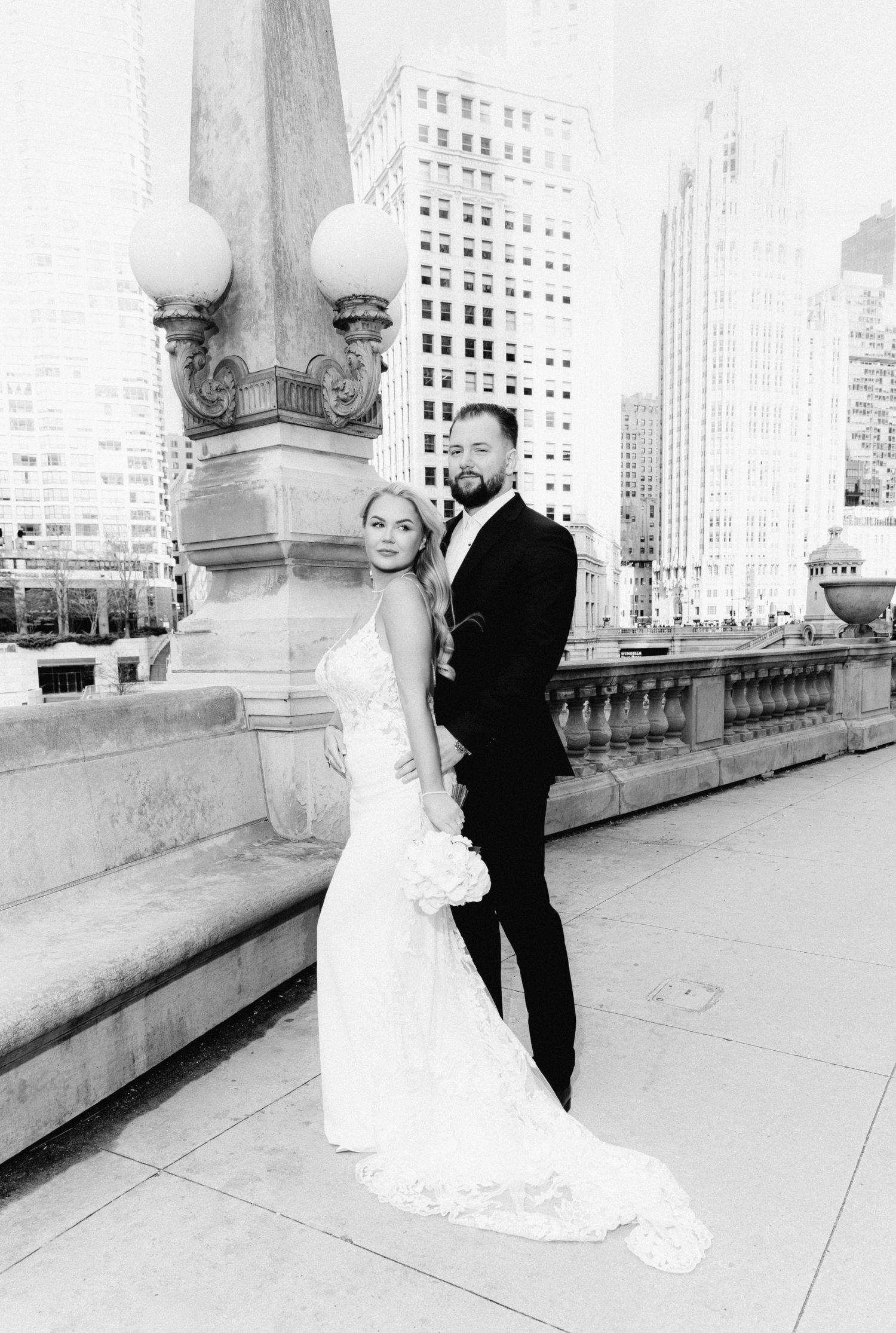Black and white photo of bride and groom posing on a Chicago bridge with skyscrapers behind them.