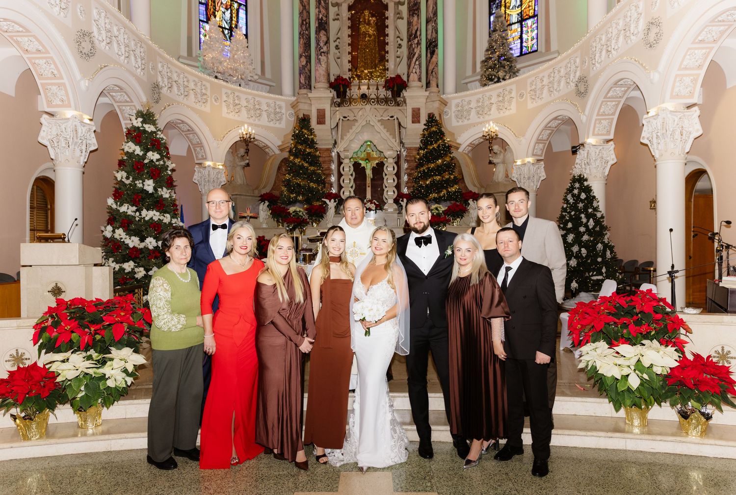 Bride, groom, and family posing together in a beautifully decorated Christmas church with poinsettias and ornate details.
