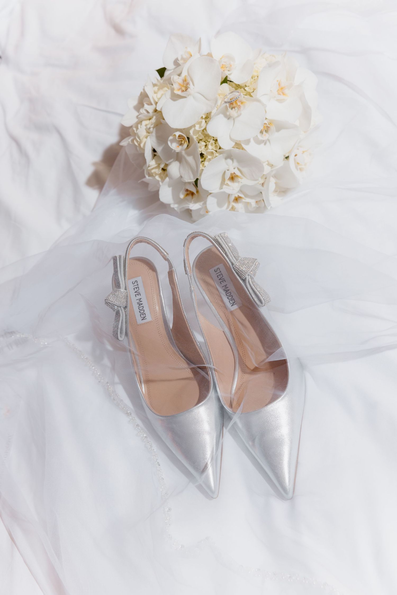 Silver Steve Madden slingback heels and white orchid bridal bouquet arranged on a flowing white wedding veil.