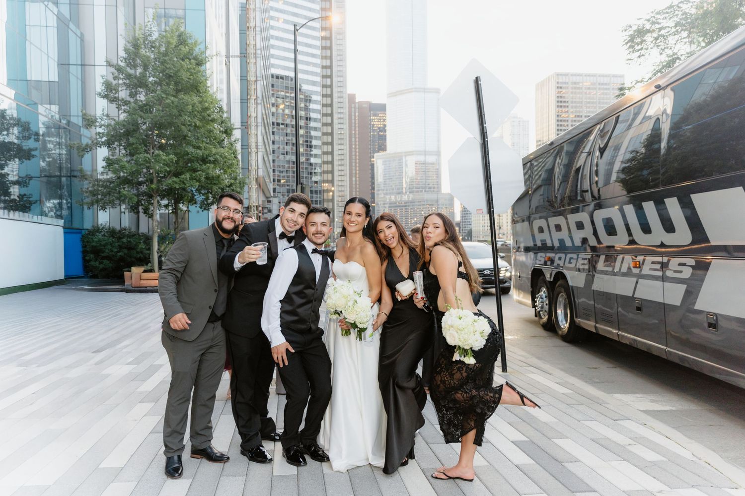Wedding party group celebrating outside with bouquets and city buildings in the background.