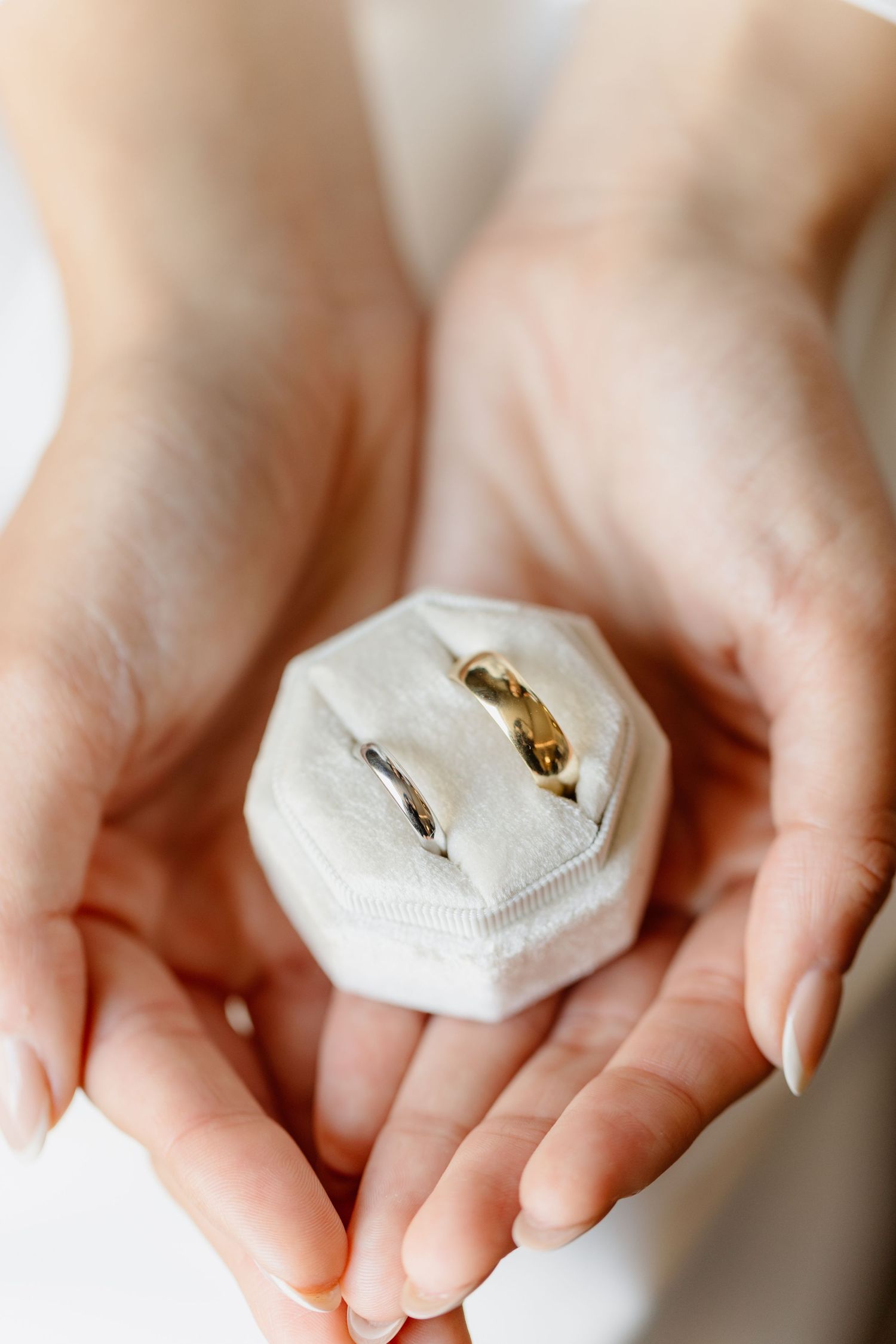 Bride holding white velvet ring box containing two wedding bands, one silver and one gold.