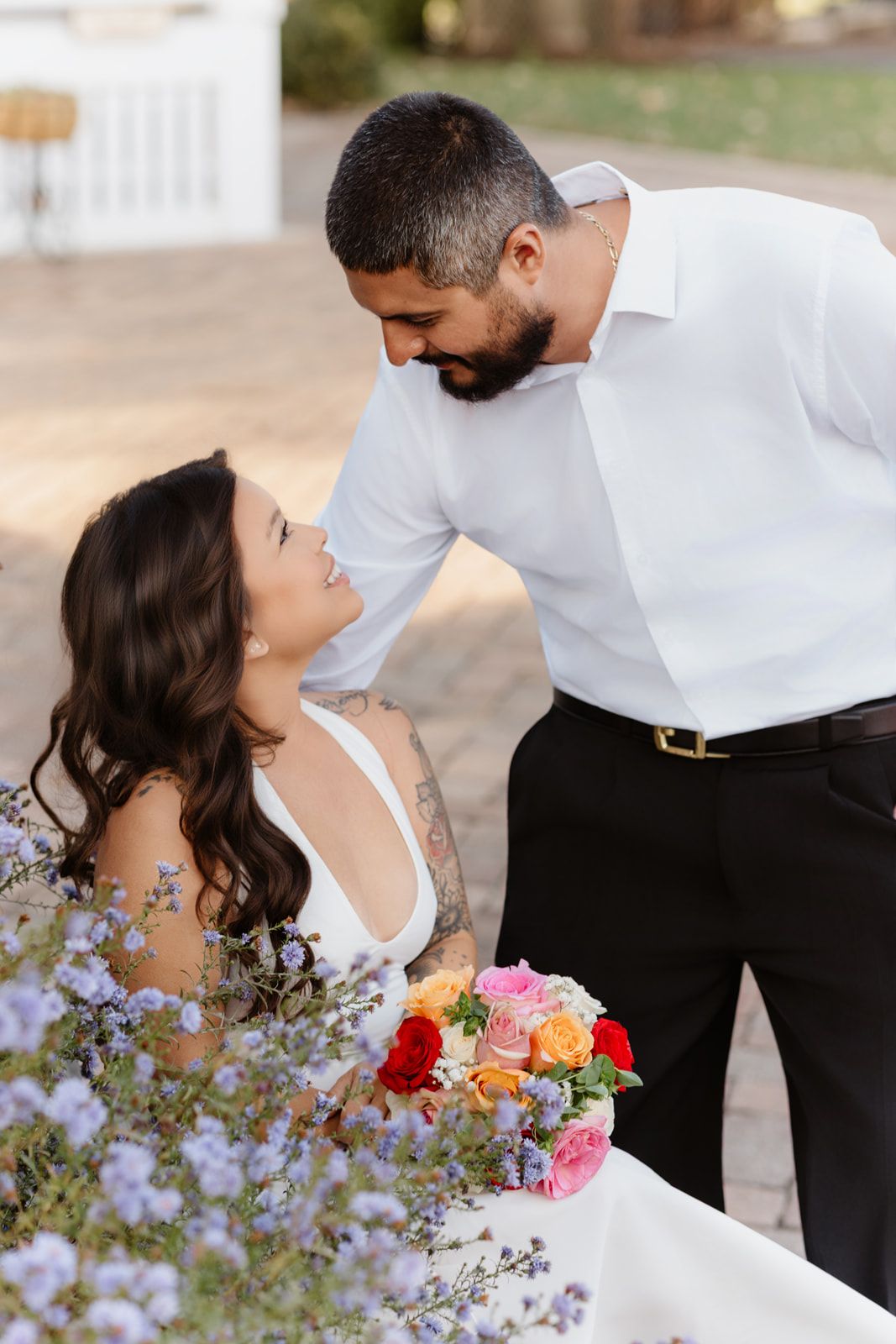 Bride gazes up lovingly at groom while holding vibrant bouquet surrounded by purple wildflowers.