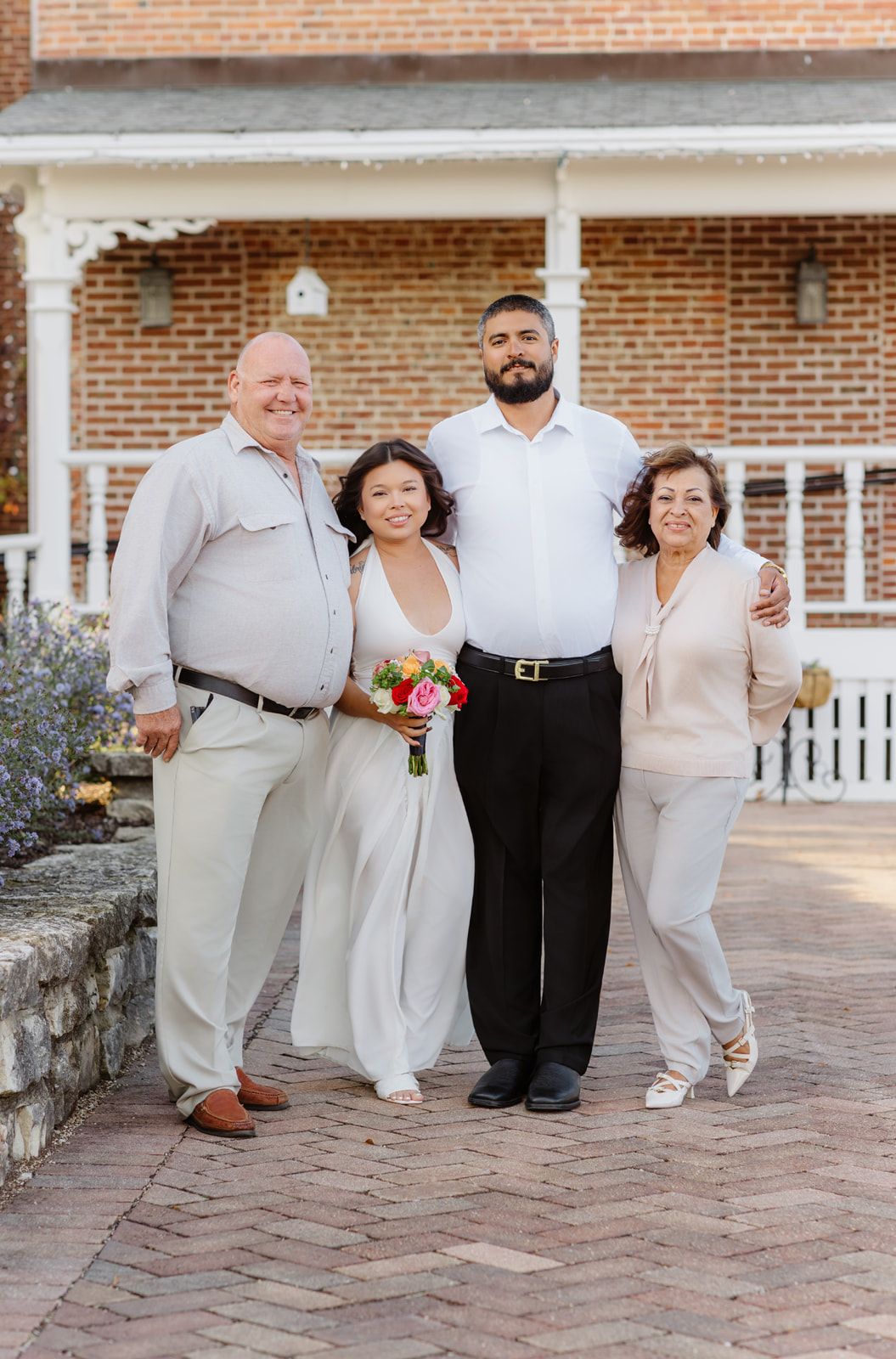 Bride and groom pose with family on brick pathway outside historic venue on wedding day.