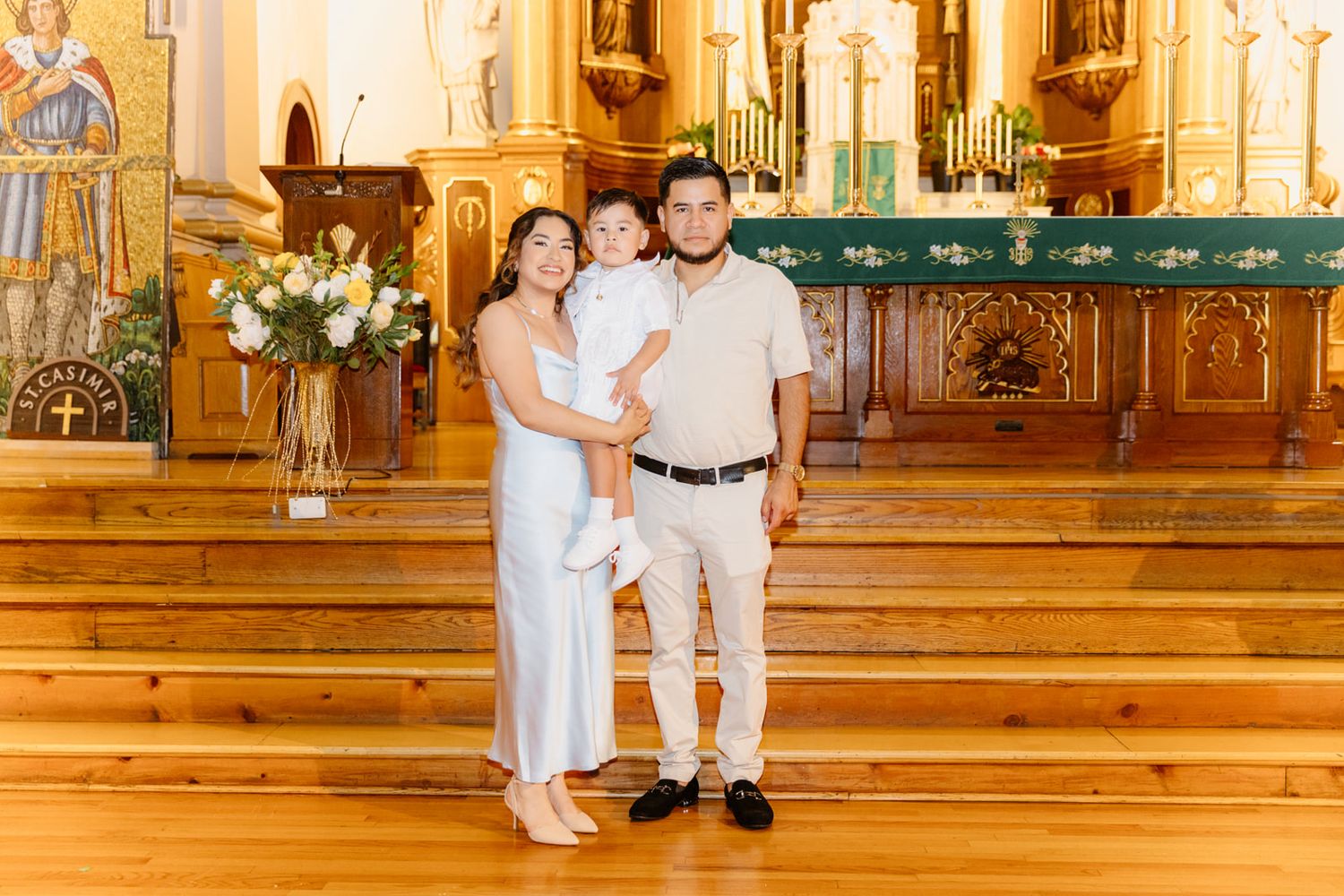 Family posing together in a beautiful church interior with wooden floors and golden altar during a baptism ceremony.