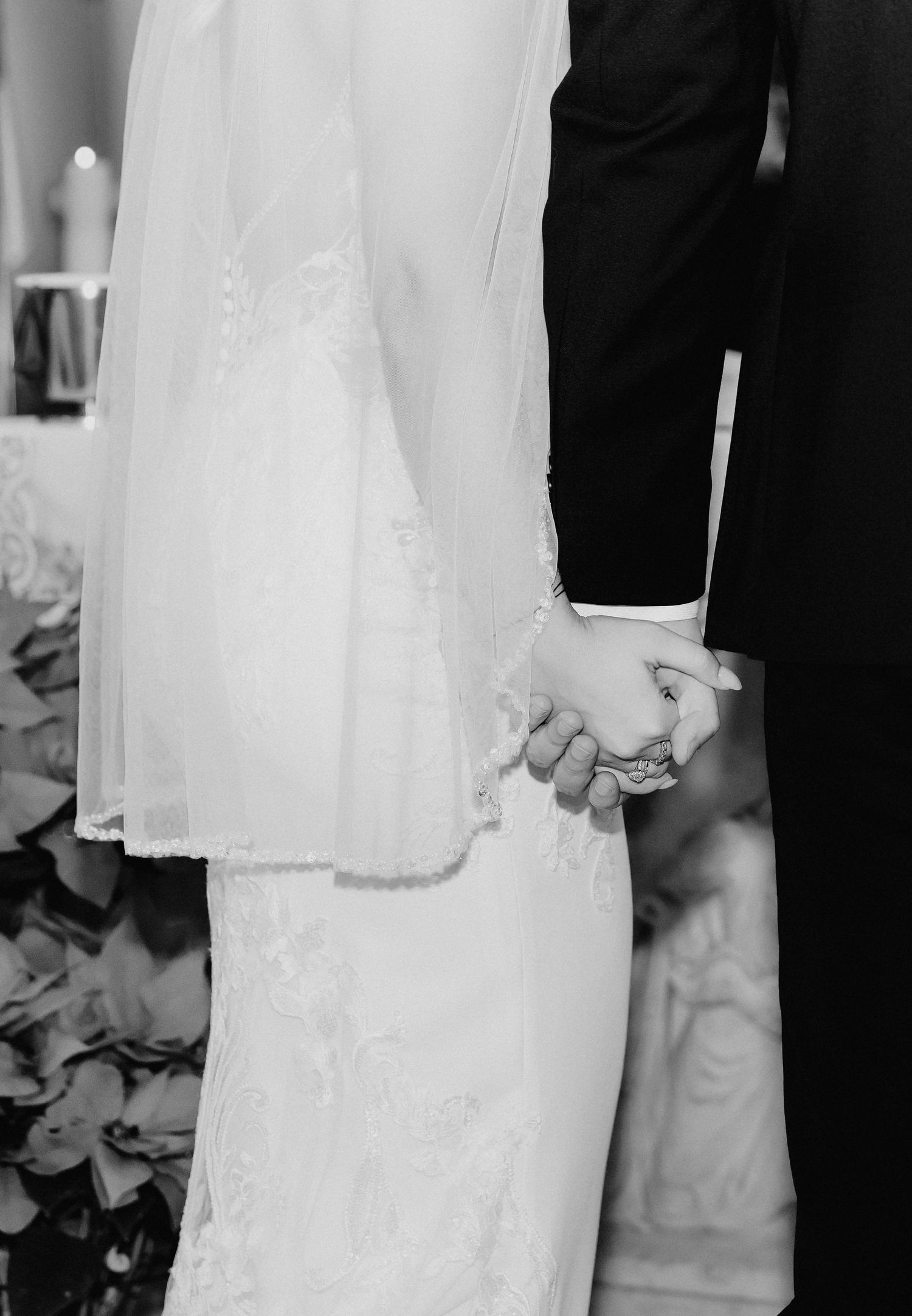 Black and white photo of bride and groom holding hands during wedding ceremony.