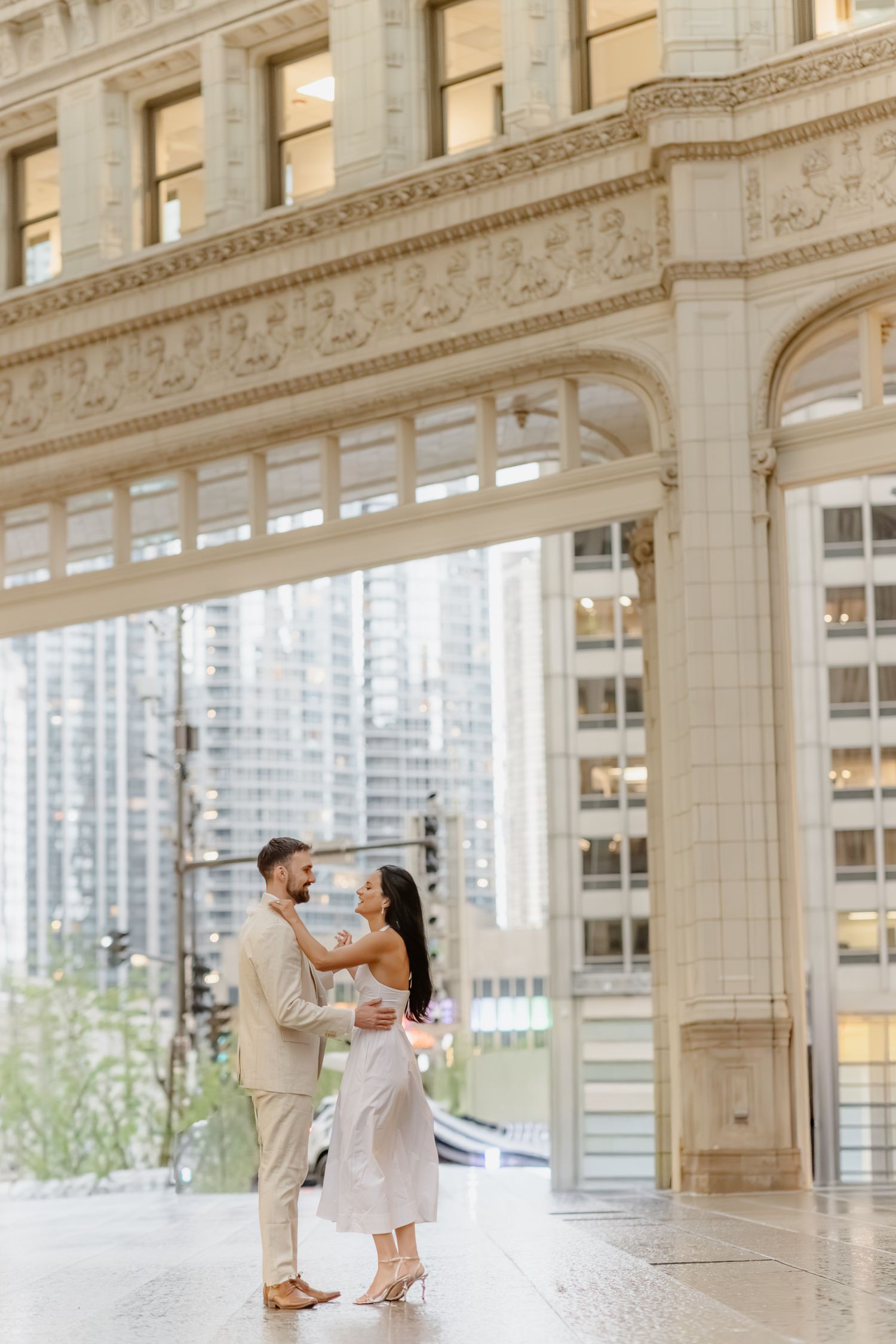 Couple dancing together beneath ornate white marble arches with city skyline backdrop.