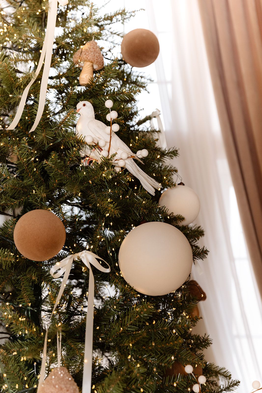 Close-up of a Christmas tree decorated with white dove ornament, beige baubles, and ribbon accents.