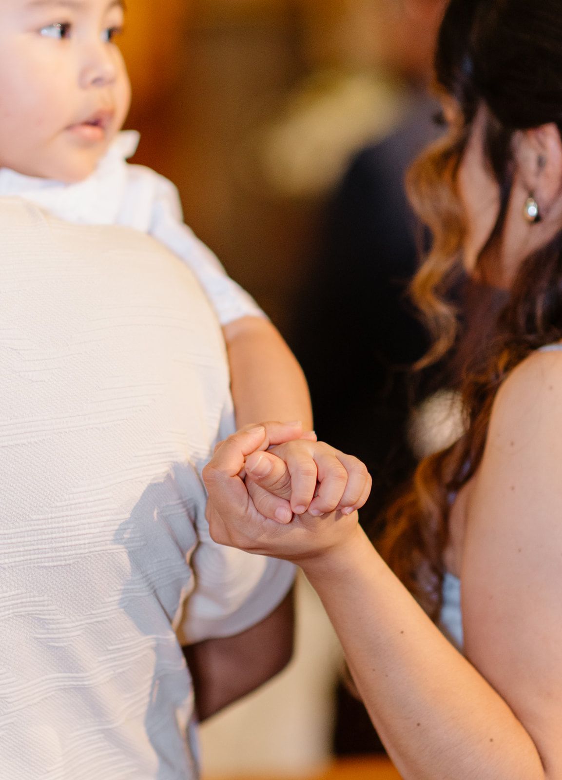 A woman gently holds a baby's hand during a tender moment at a formal event.
