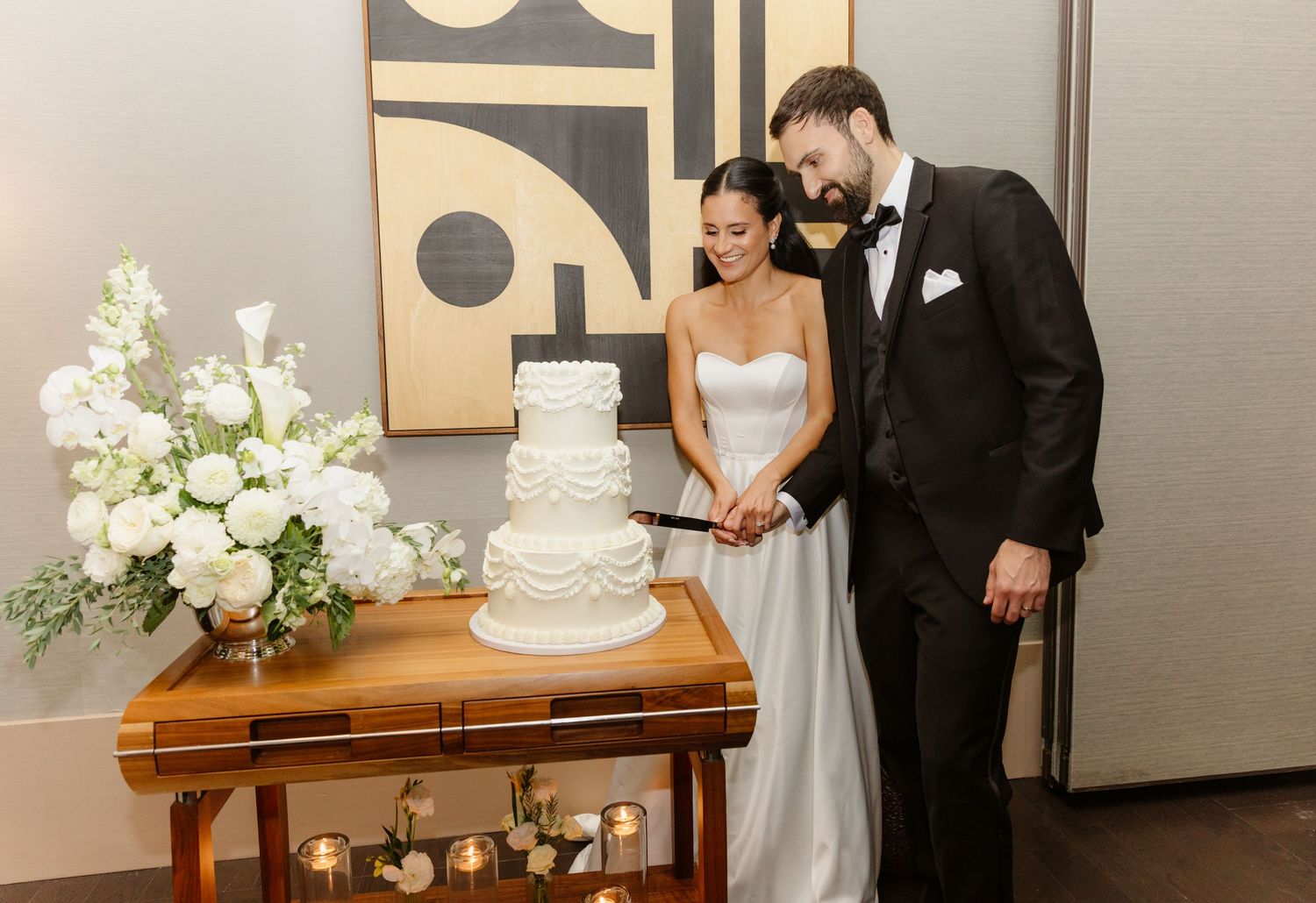 Bride and groom cutting their elegant white tiered wedding cake at a modern indoor reception venue.