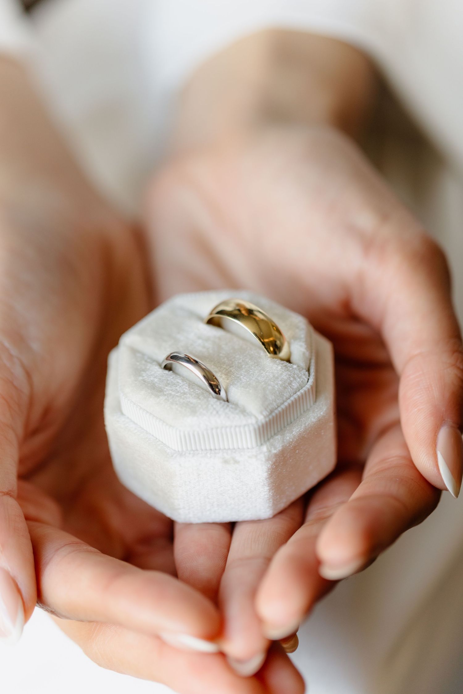 Hands holding a white velvet ring box with two wedding bands, one gold and one silver, for a wedding ceremony.