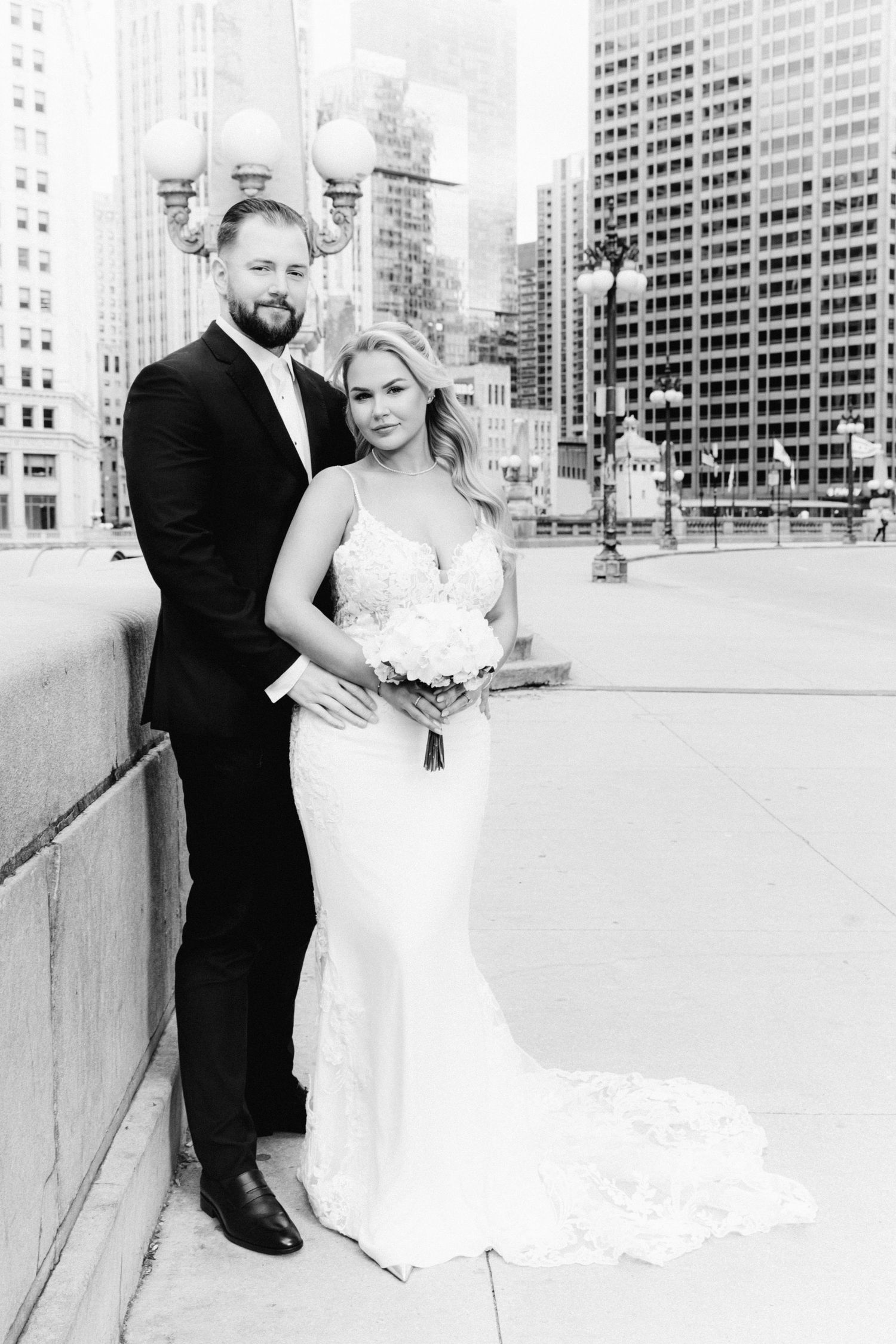 Black and white wedding portrait of couple posing on Chicago bridge with stunning city skyline backdrop.