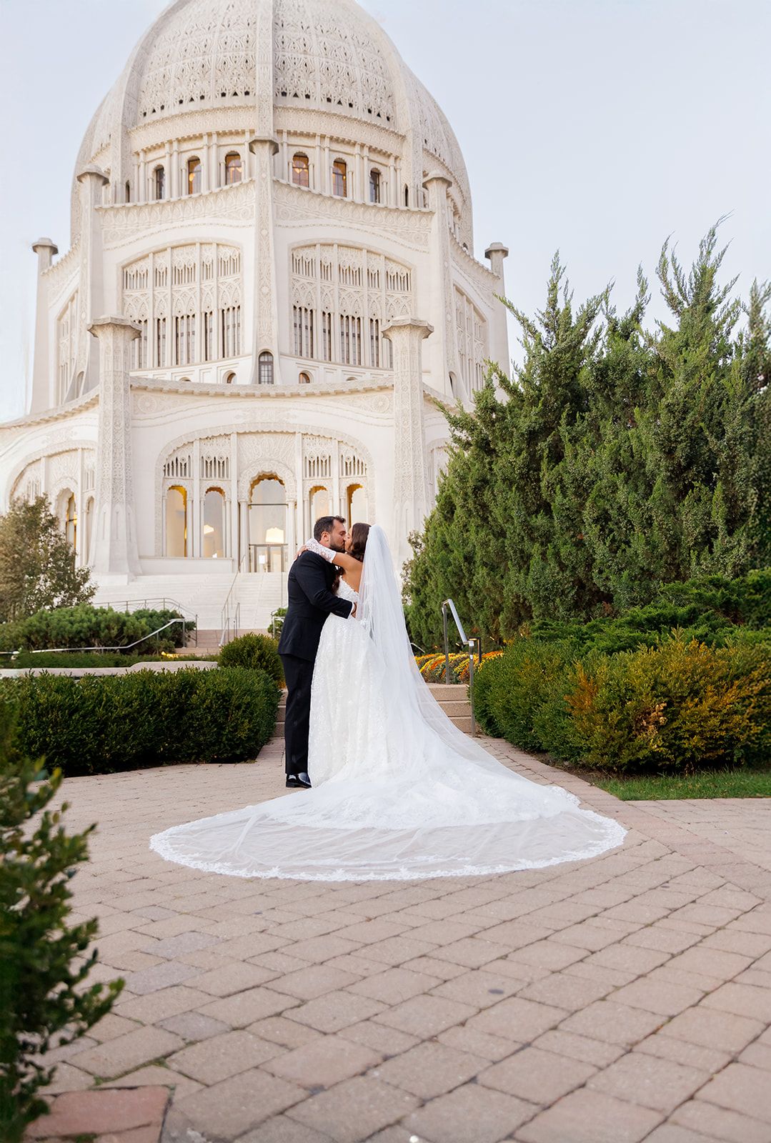 Bride and groom kissing in front of the Bahai Temple in Wilmette, Illinois, with a long cathedral veil spread on the ground.