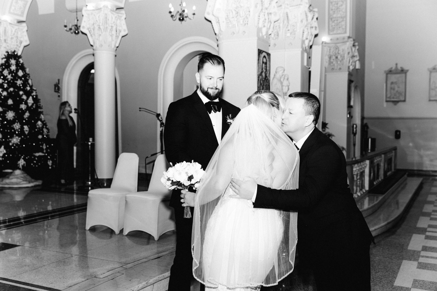 Black and white wedding photo of bride and groom with officiant during church ceremony.