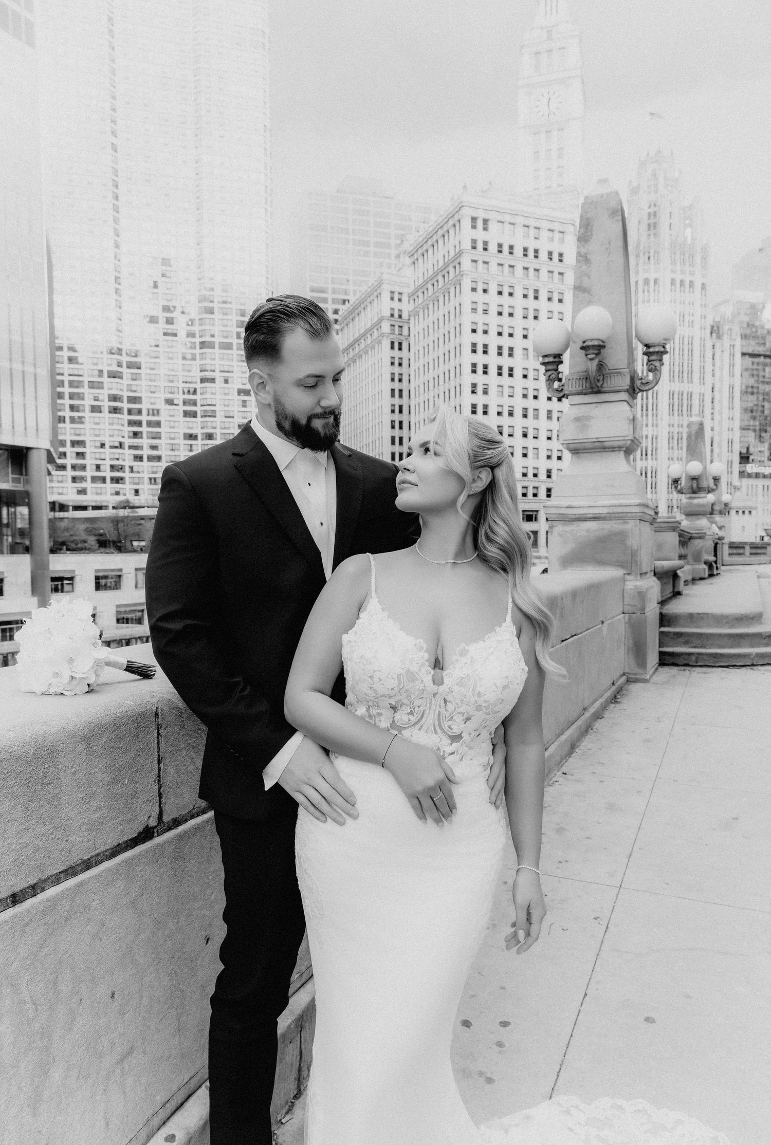 Black and white portrait of bride and groom embracing on Chicago bridge with city skyline background.