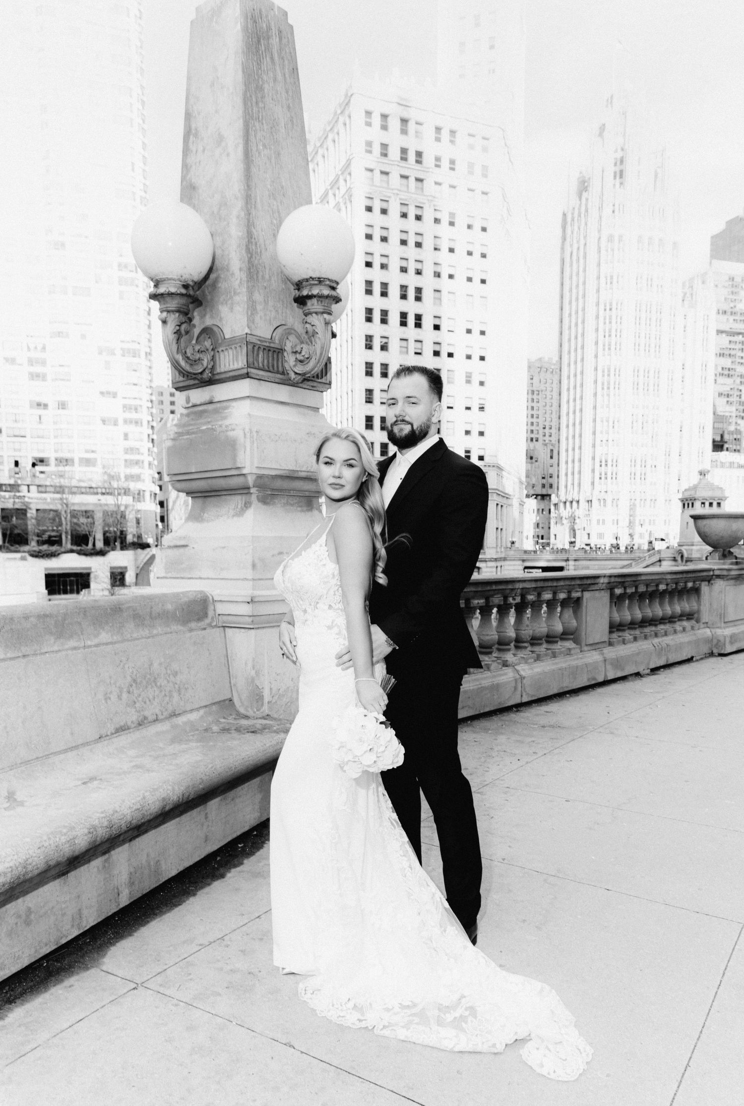 Black and white wedding portrait of couple standing by ornate lamp post on Chicago bridge.