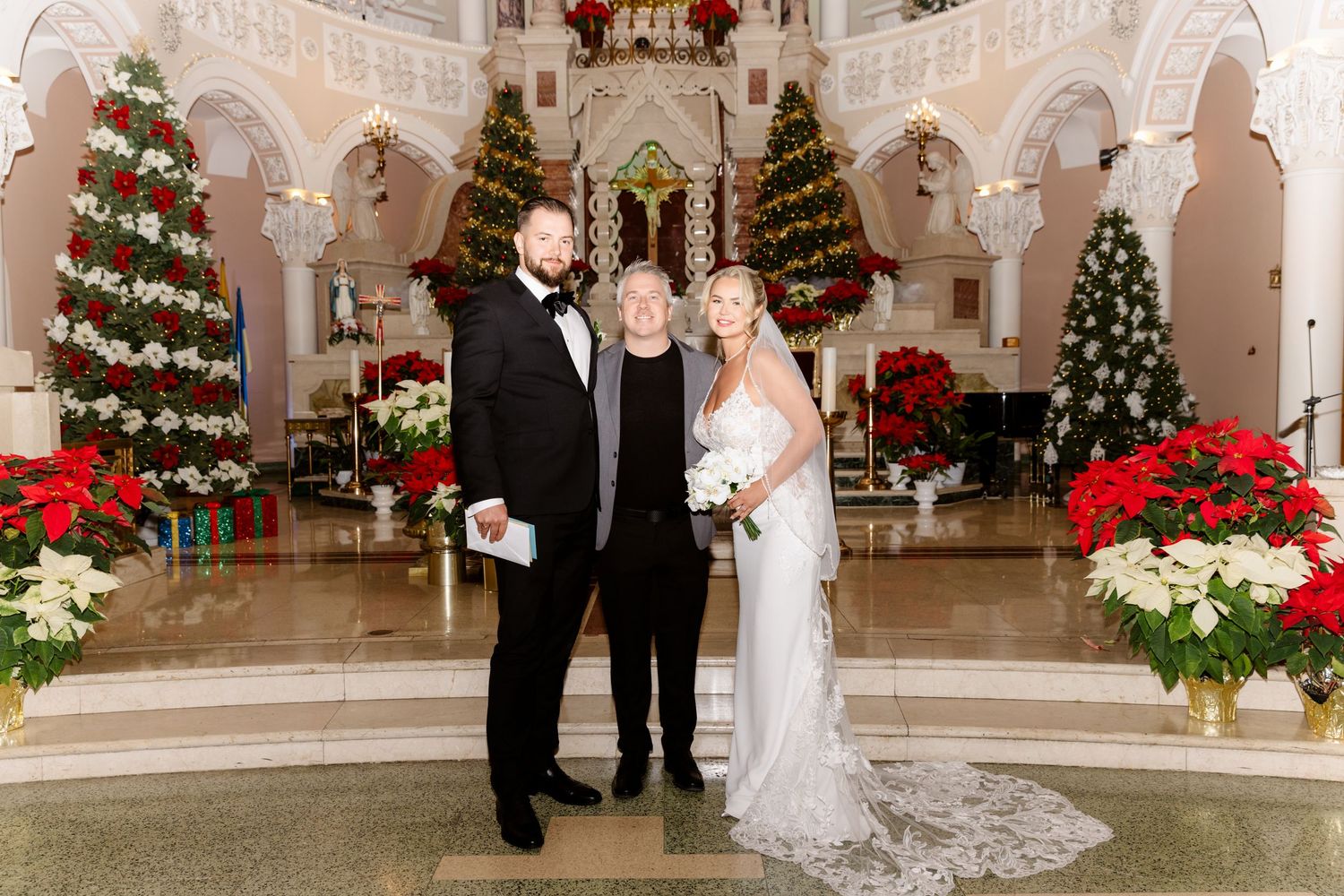 Bride and groom posing with older male guest in stunning Christmas-decorated church interior.