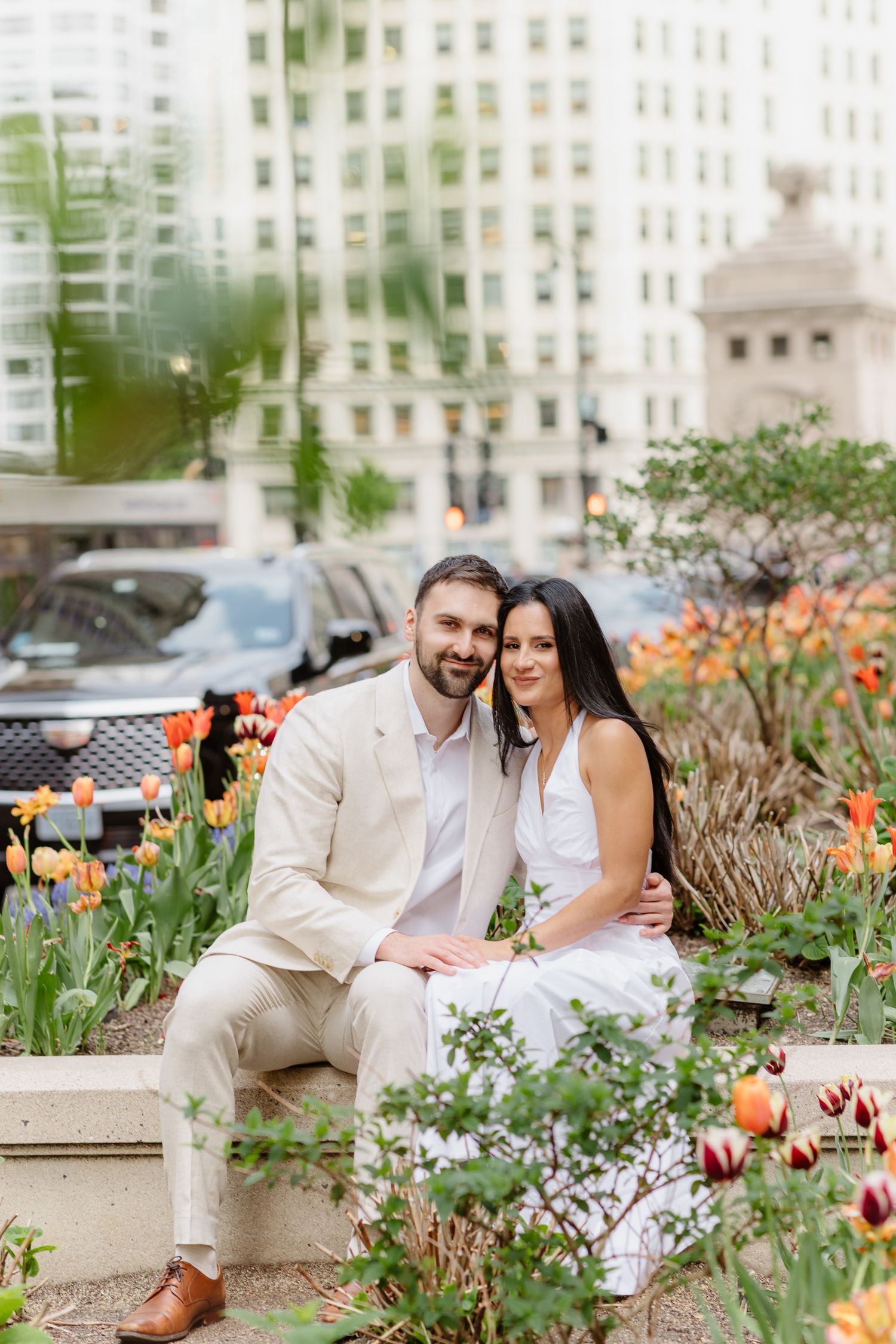 Smiling couple sits together among colorful tulips with Chicago city buildings reflected behind them.