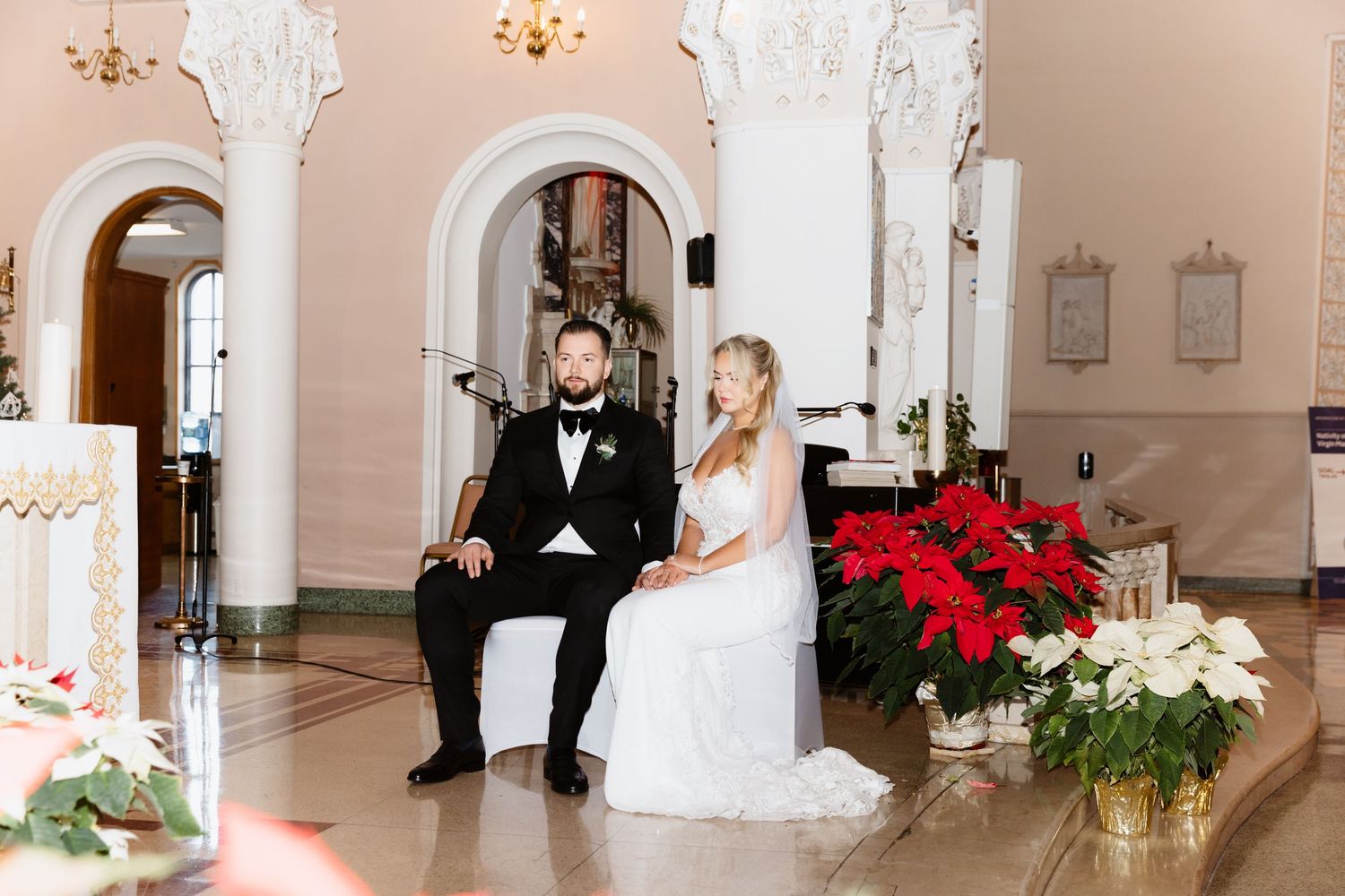 Elegant bride and groom seated at altar of beautifully decorated church during winter wedding.