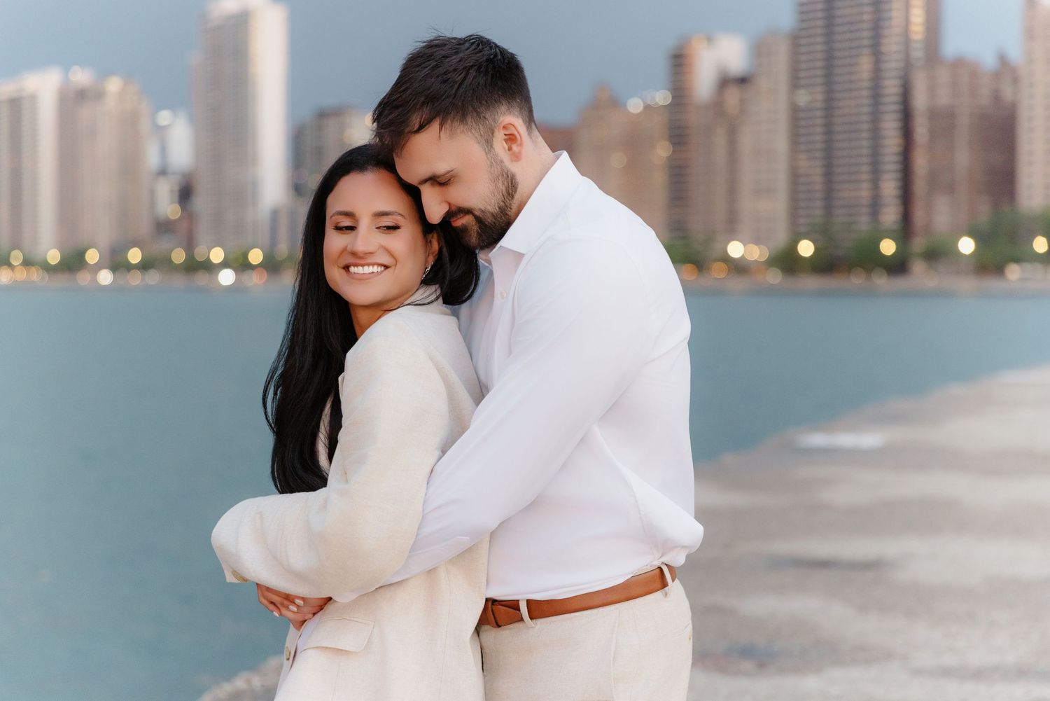 Close-up of smiling couple embracing on Chicago lakefront with blurred skyline background.