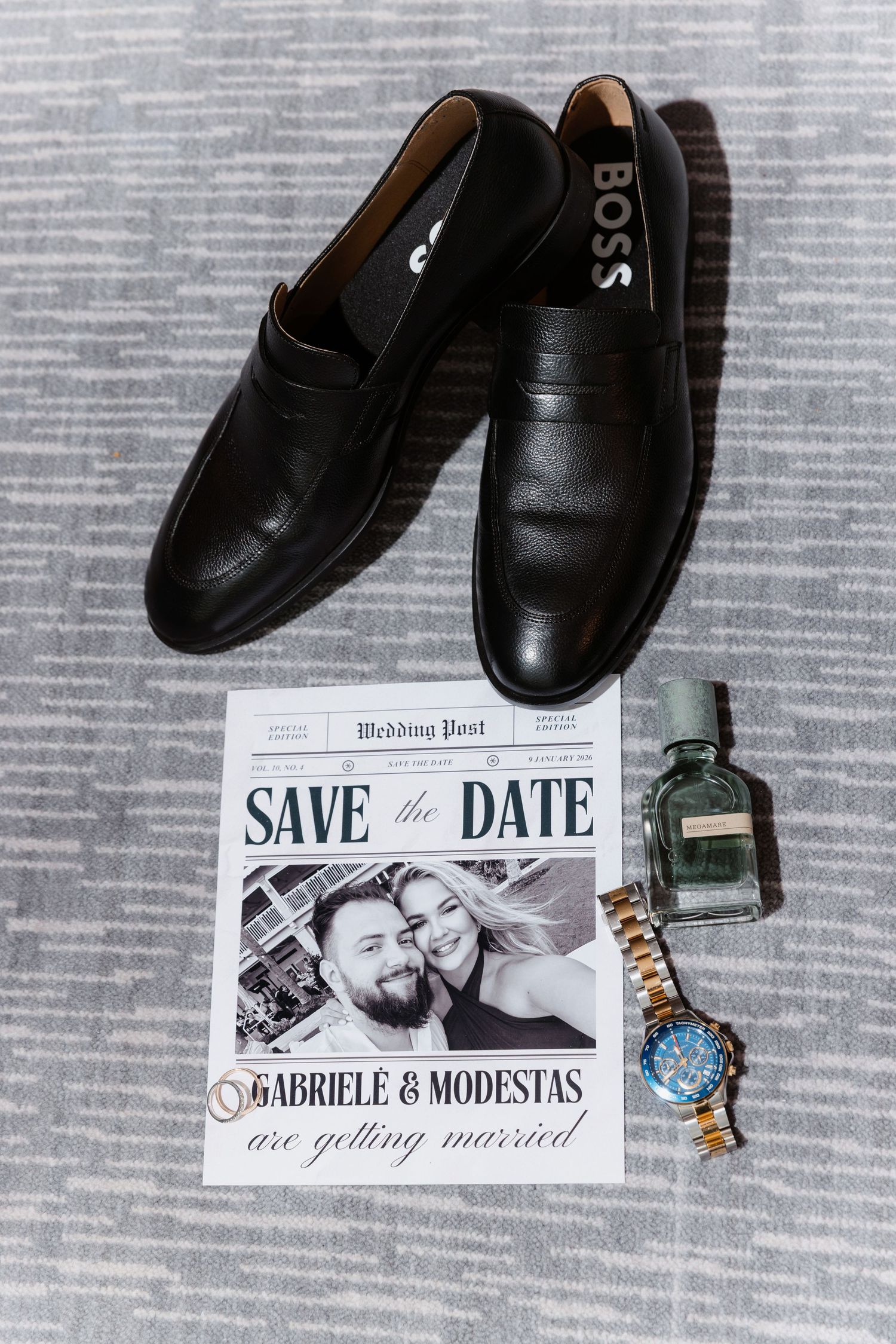 Groom wedding flat lay with BOSS loafers, save the date card, cologne, and gold watch on gray rug.