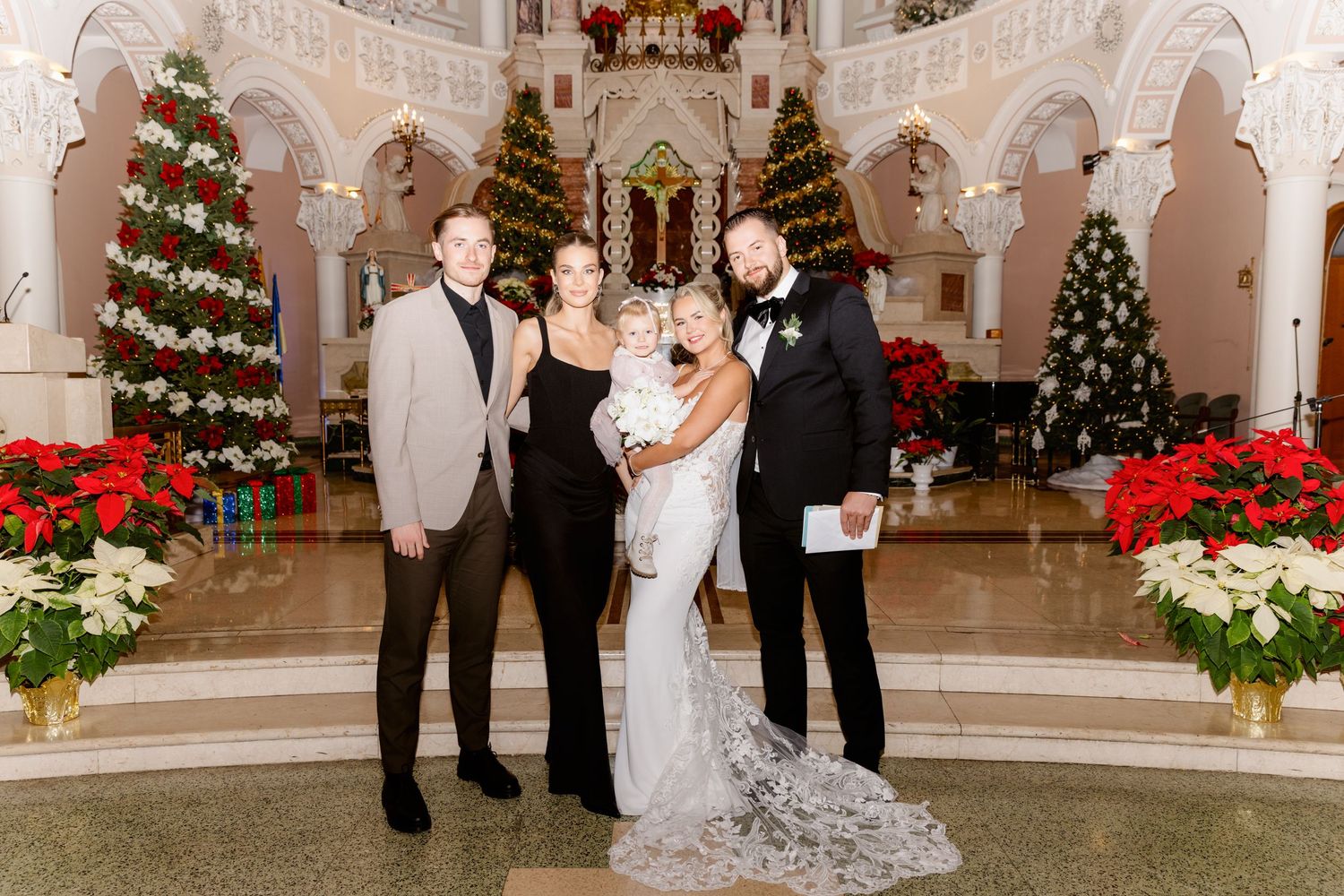 Bride and groom with three guests including a baby pose in a holiday-decorated church interior.