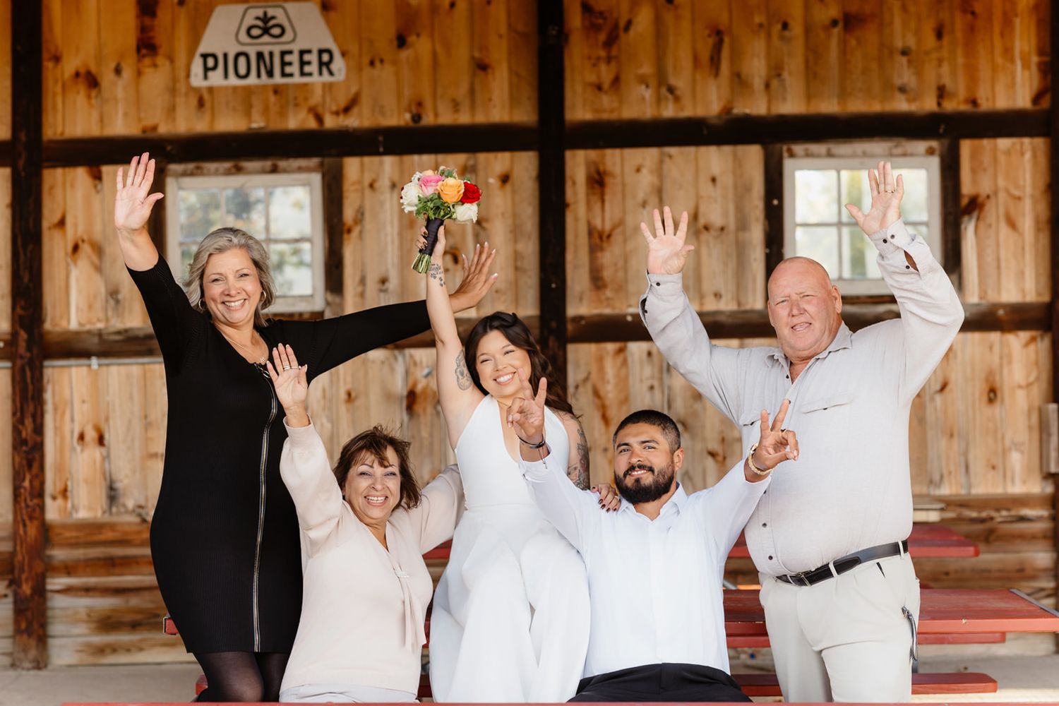 Joyful wedding party of five celebrates with raised hands inside a rustic Pioneer barn venue.