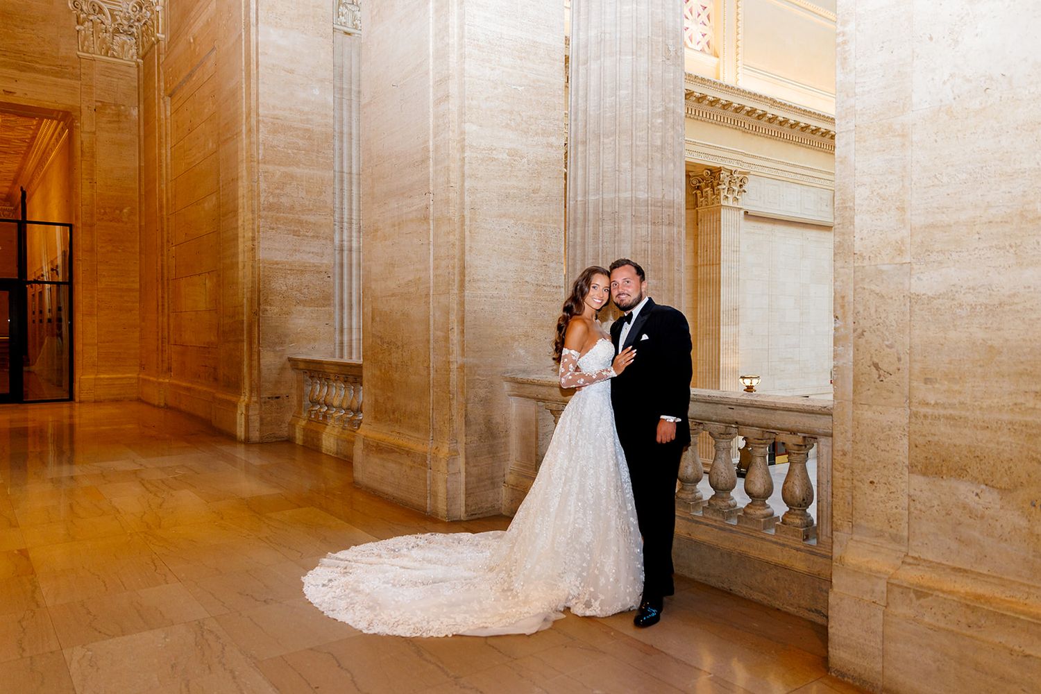 Bride and groom embrace in an elegant marble corridor with ornate columns during their wedding day.