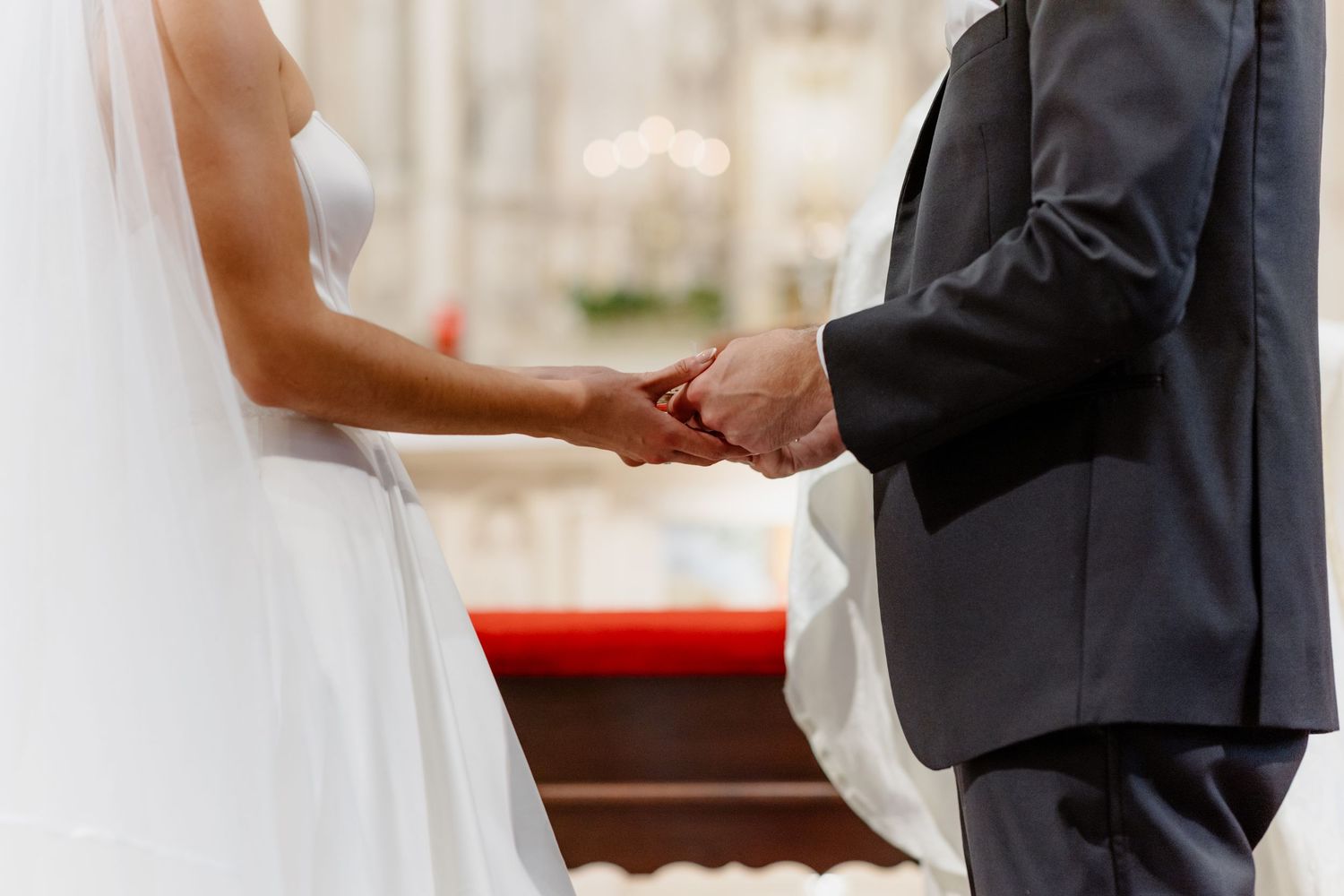 Bride and groom exchange rings holding hands during elegant wedding ceremony.
