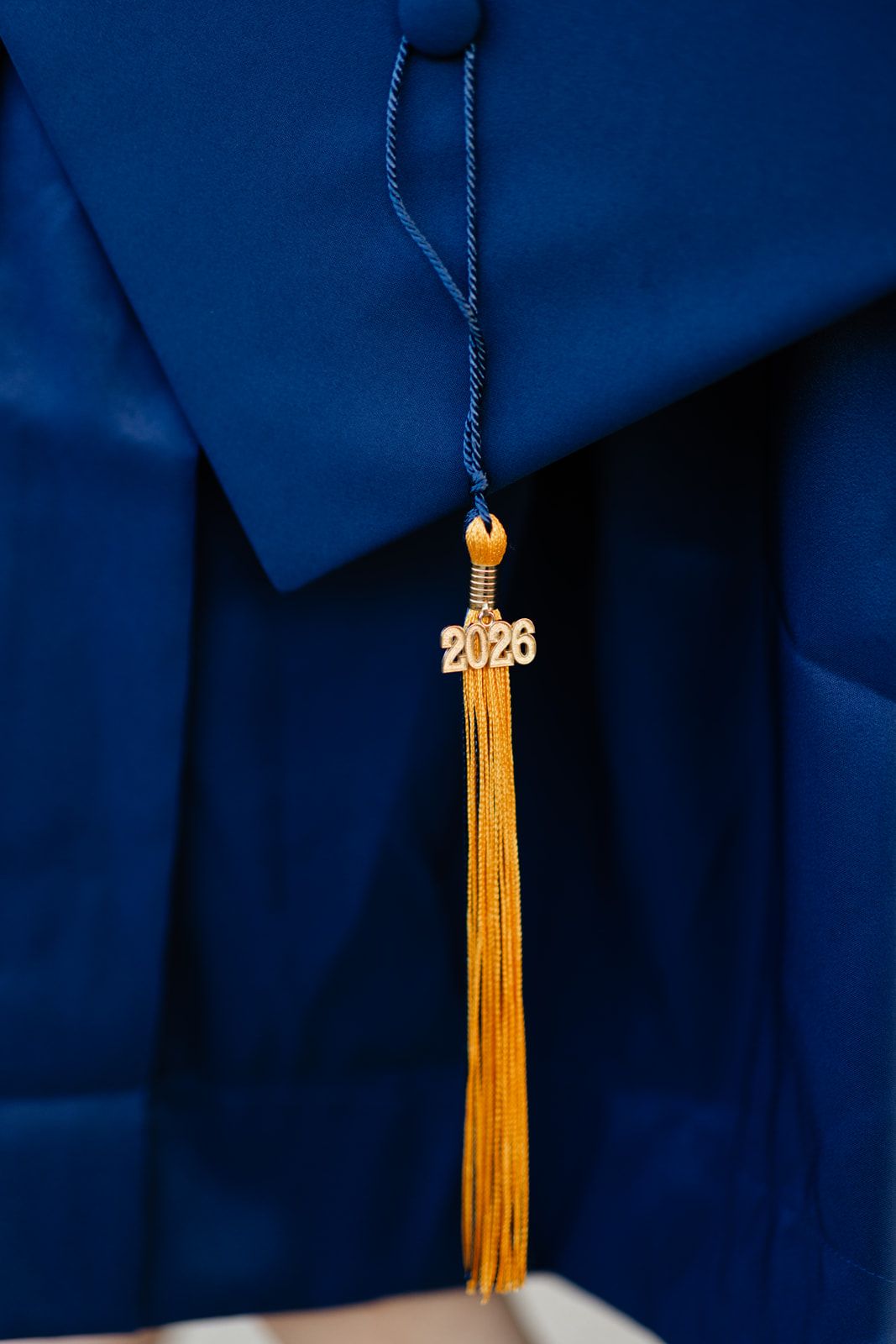 Close-up of a gold 2026 graduation tassel on a navy blue cap and gown.