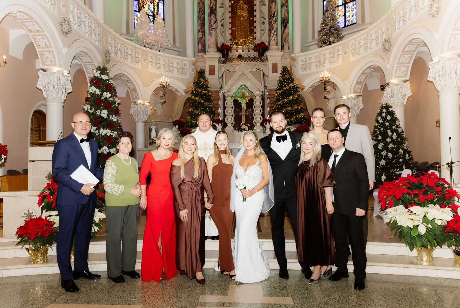 Large wedding family group portrait inside a stunning Christmas-decorated Catholic church with poinsettias and holiday trees.