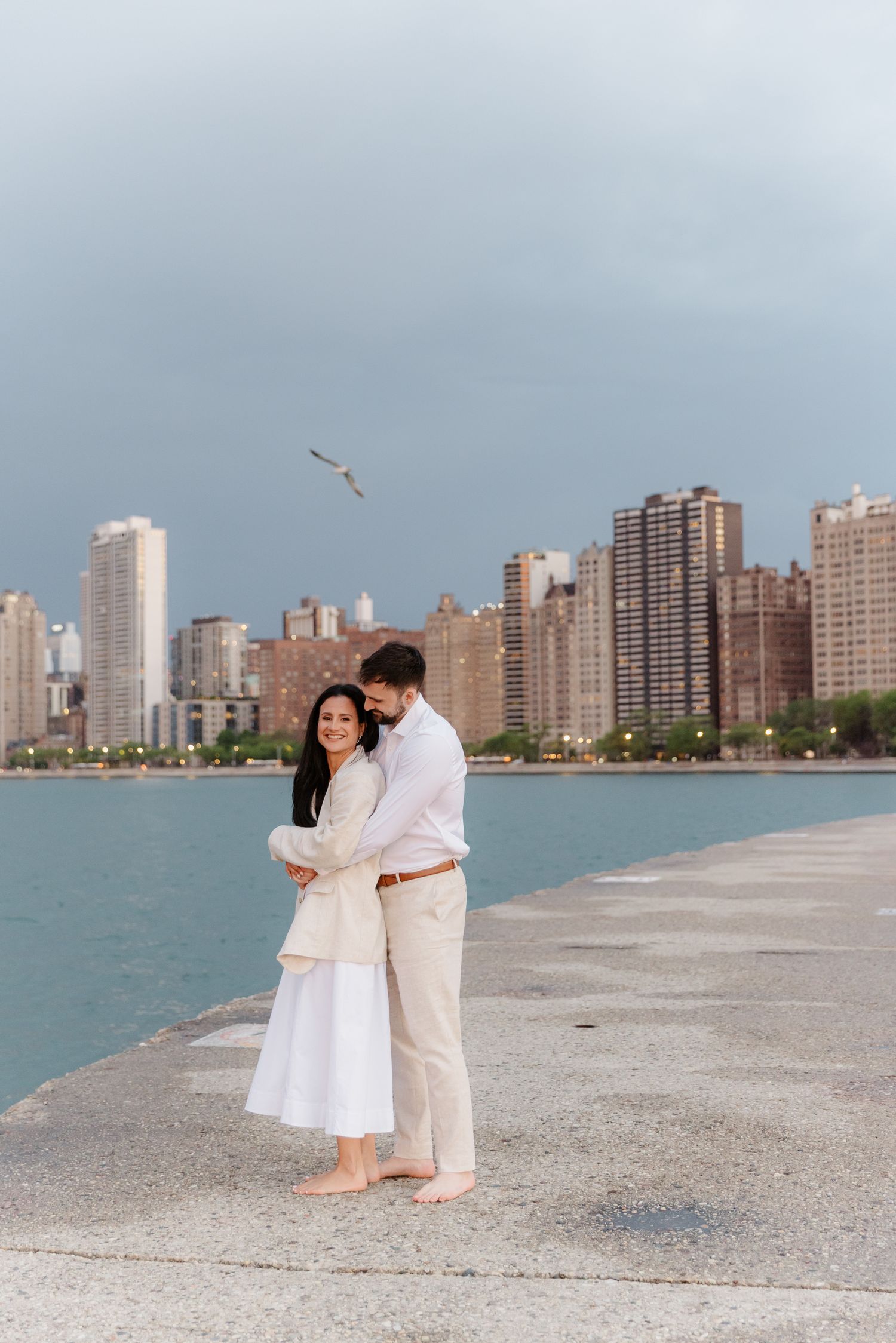 Romantic couple embracing on Chicago lakefront pier with skyline and seagull overhead.