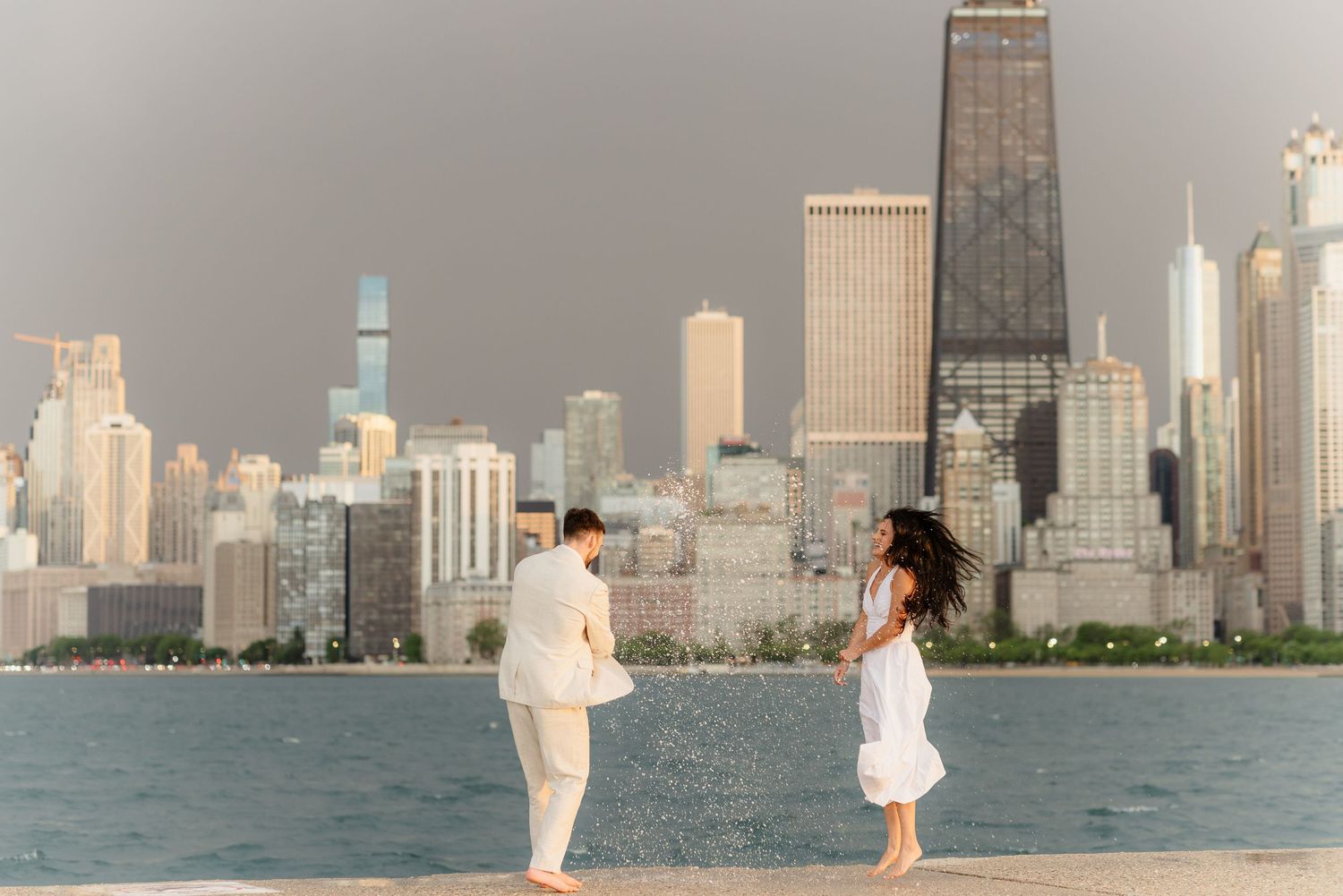 Joyful couple dancing and splashing near Lake Michigan with Chicago city skyline backdrop.