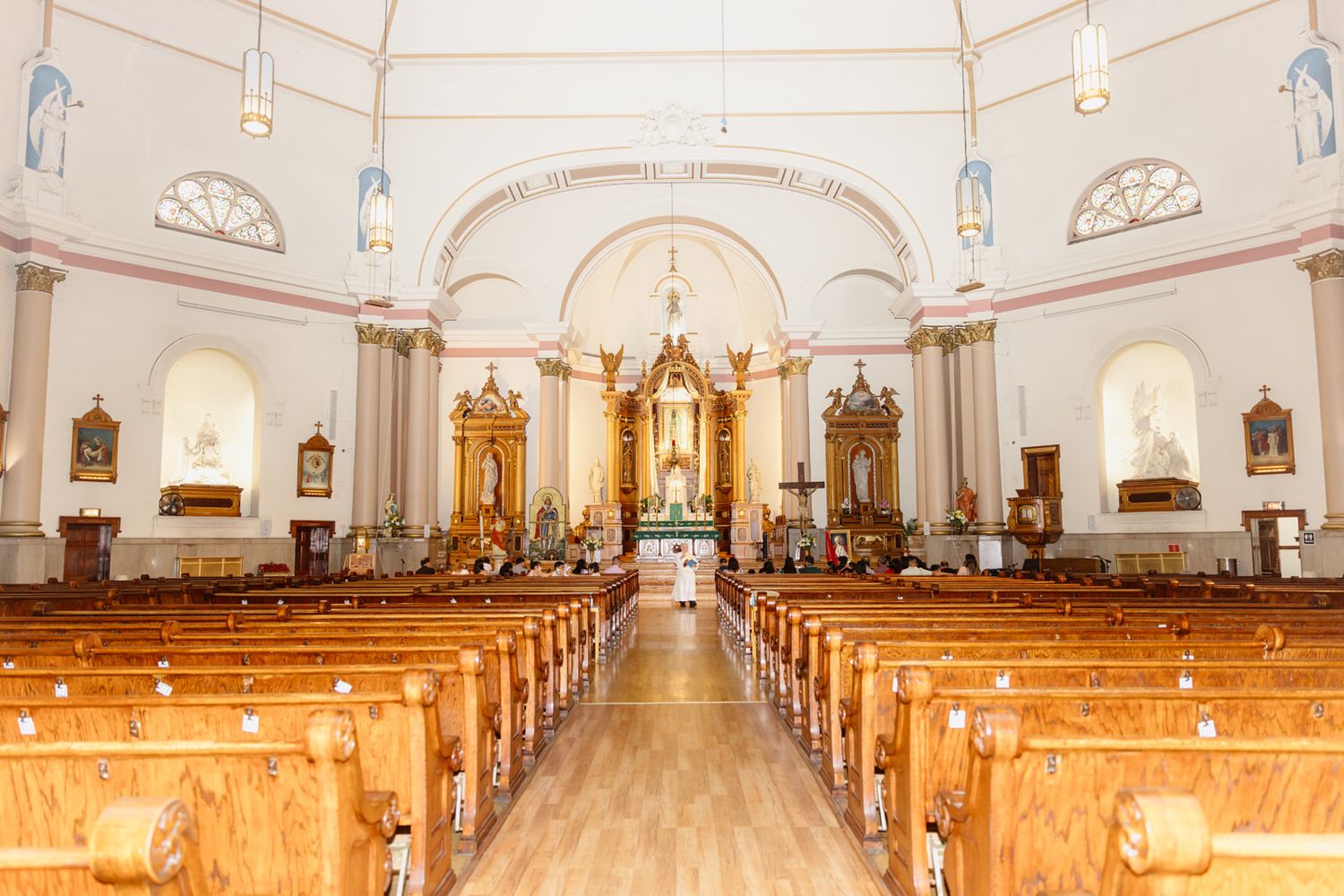 Interior of a white Catholic church with wooden pews, ornate golden altars, and arched ceilings leading to the sanctuary.