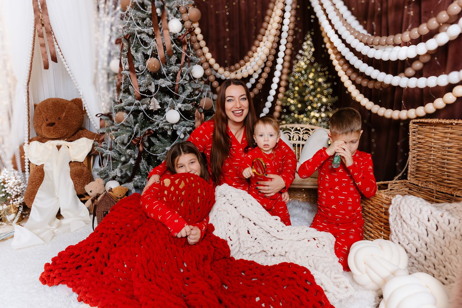 Family in matching red pajamas poses with a Christmas tree and holiday decorations in a festive studio setting.