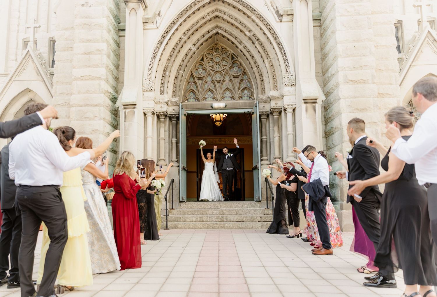 Newlyweds celebrated by guests outside ornate Gothic church entrance after wedding ceremony.