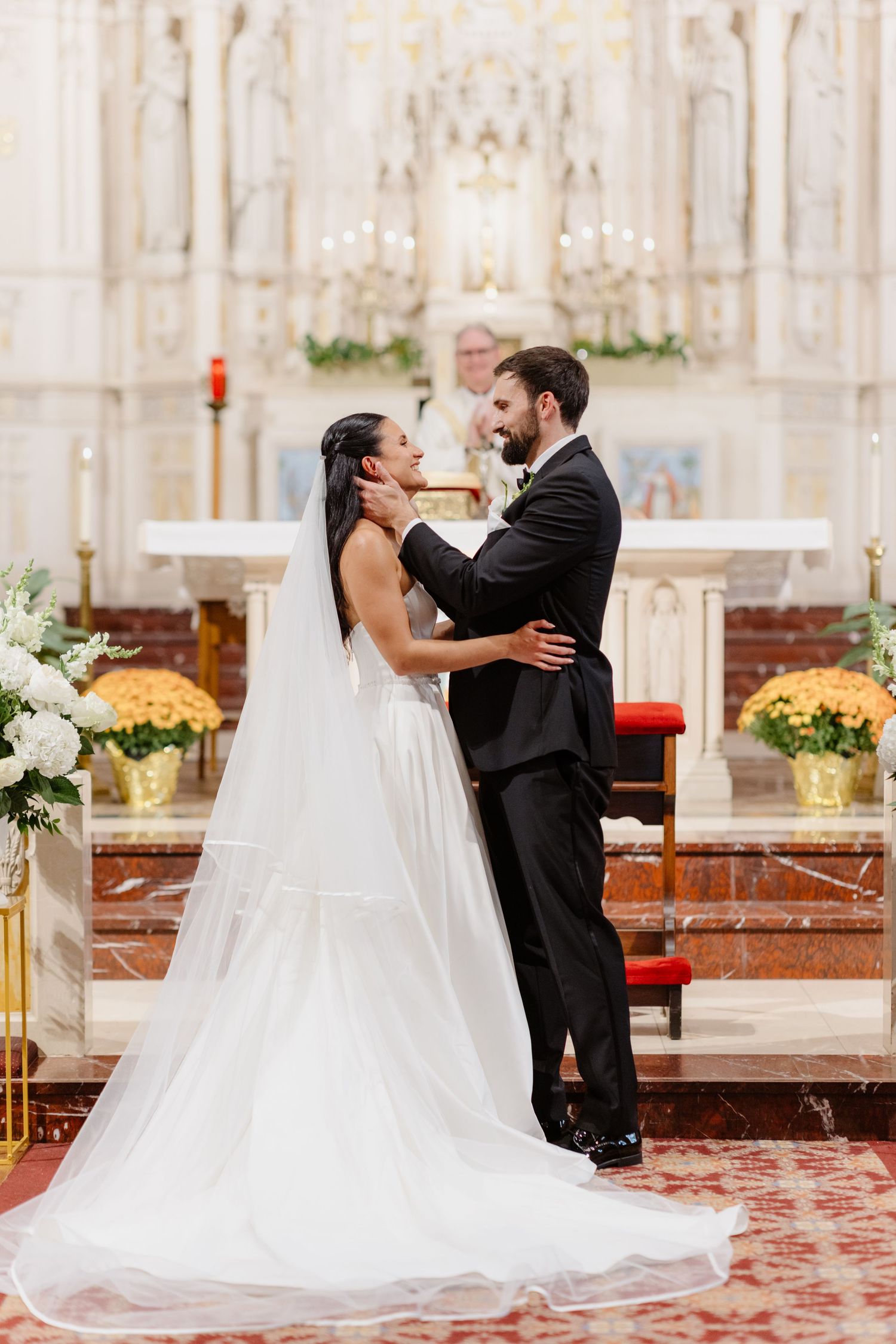 Bride and groom share romantic moment at ornate white church altar during wedding ceremony.