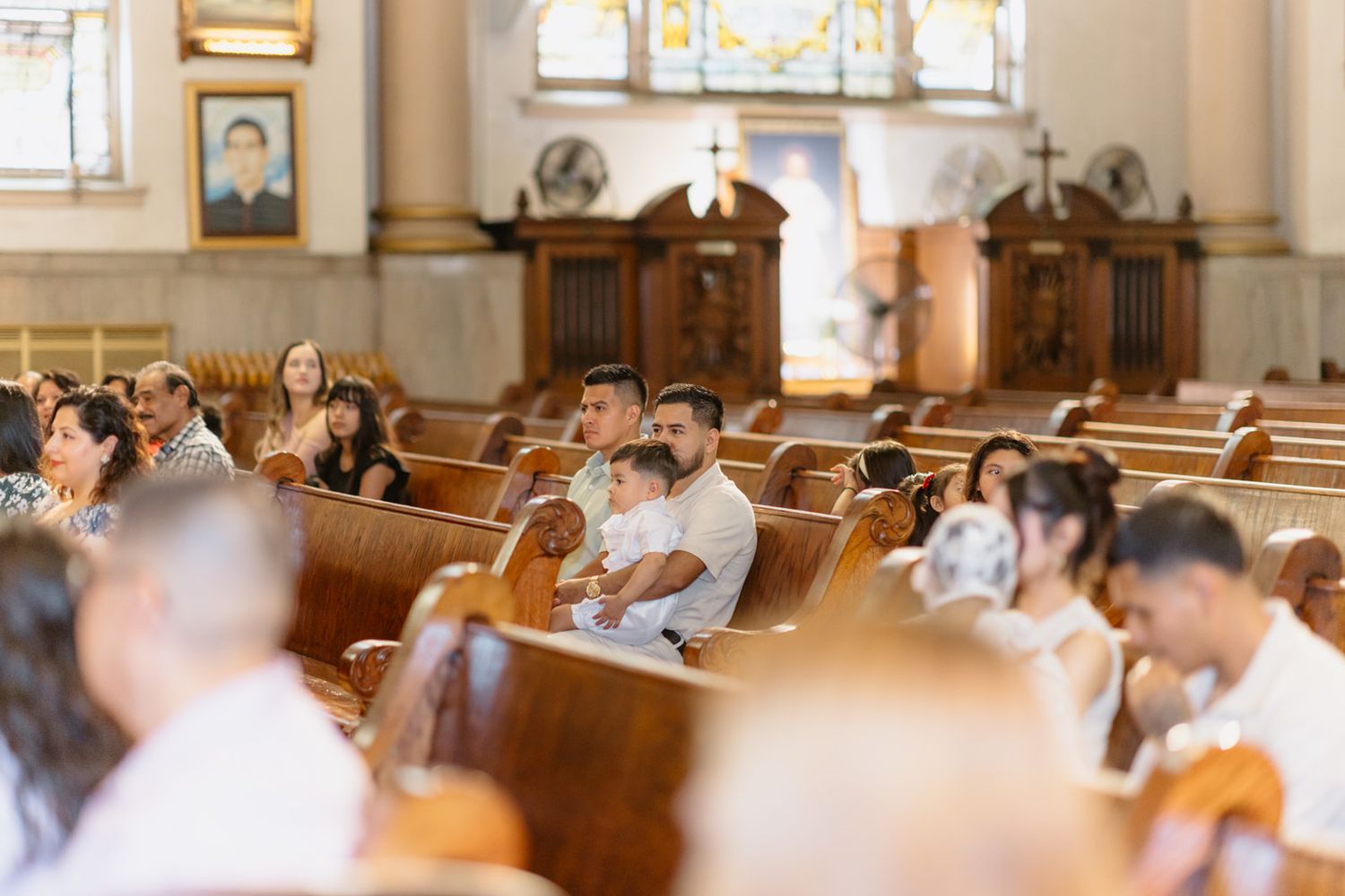 Congregation seated in wooden church pews during a religious ceremony in an ornate Catholic church.