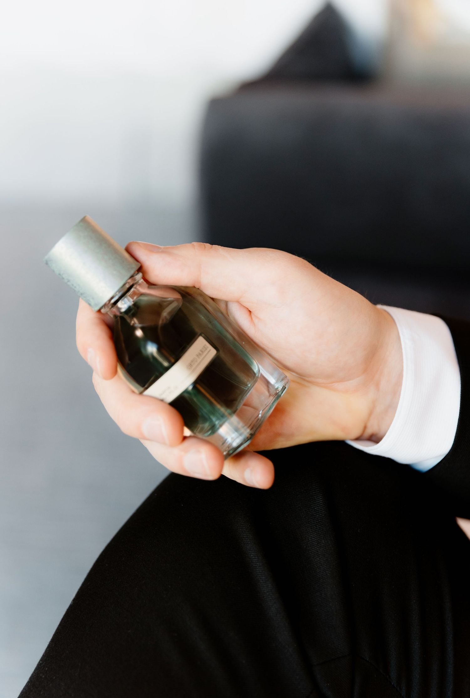 Groom holding luxury glass cologne bottle in white dress shirt sleeve before wedding ceremony.